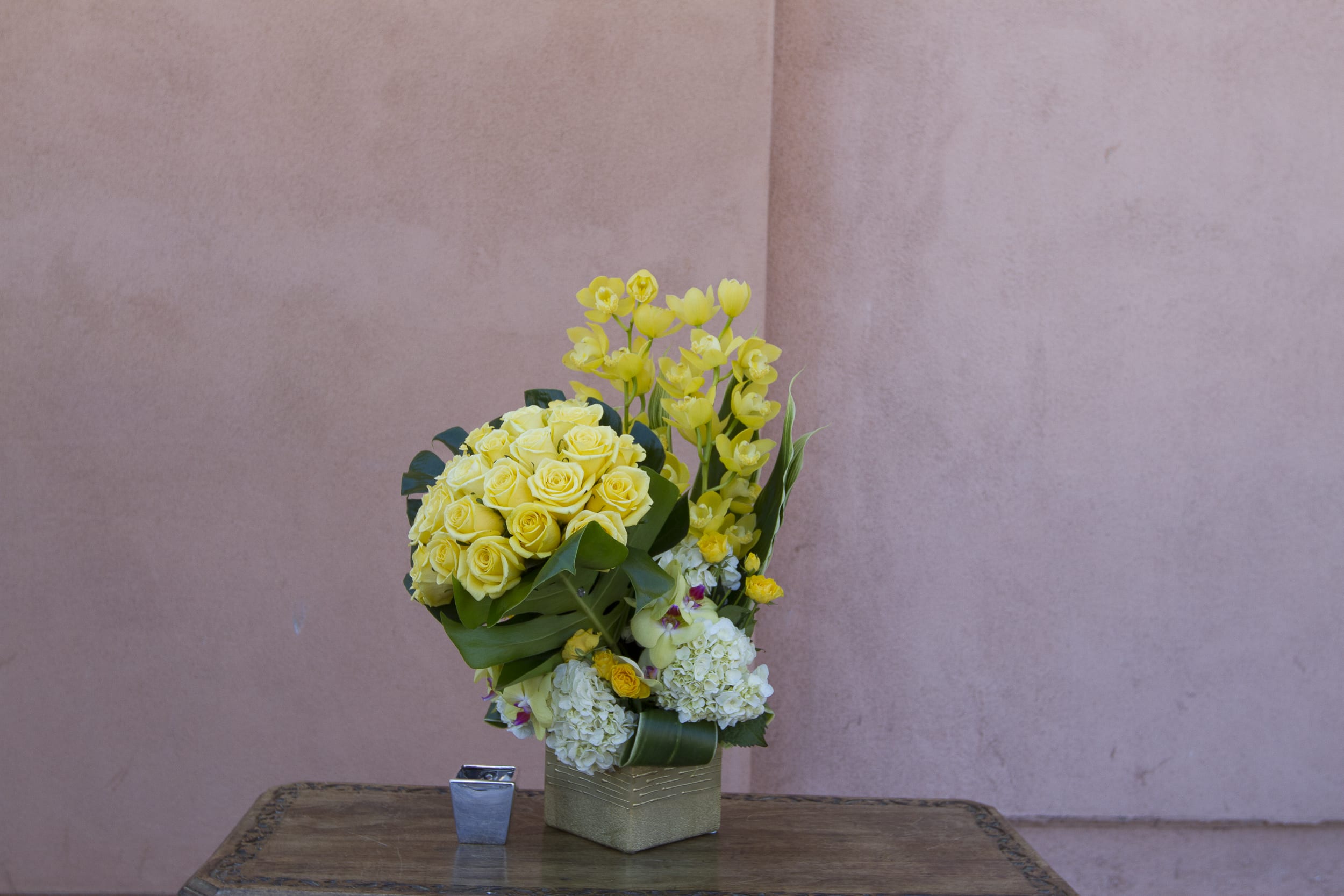 Yellow roses and orchids arranged in a square vase
