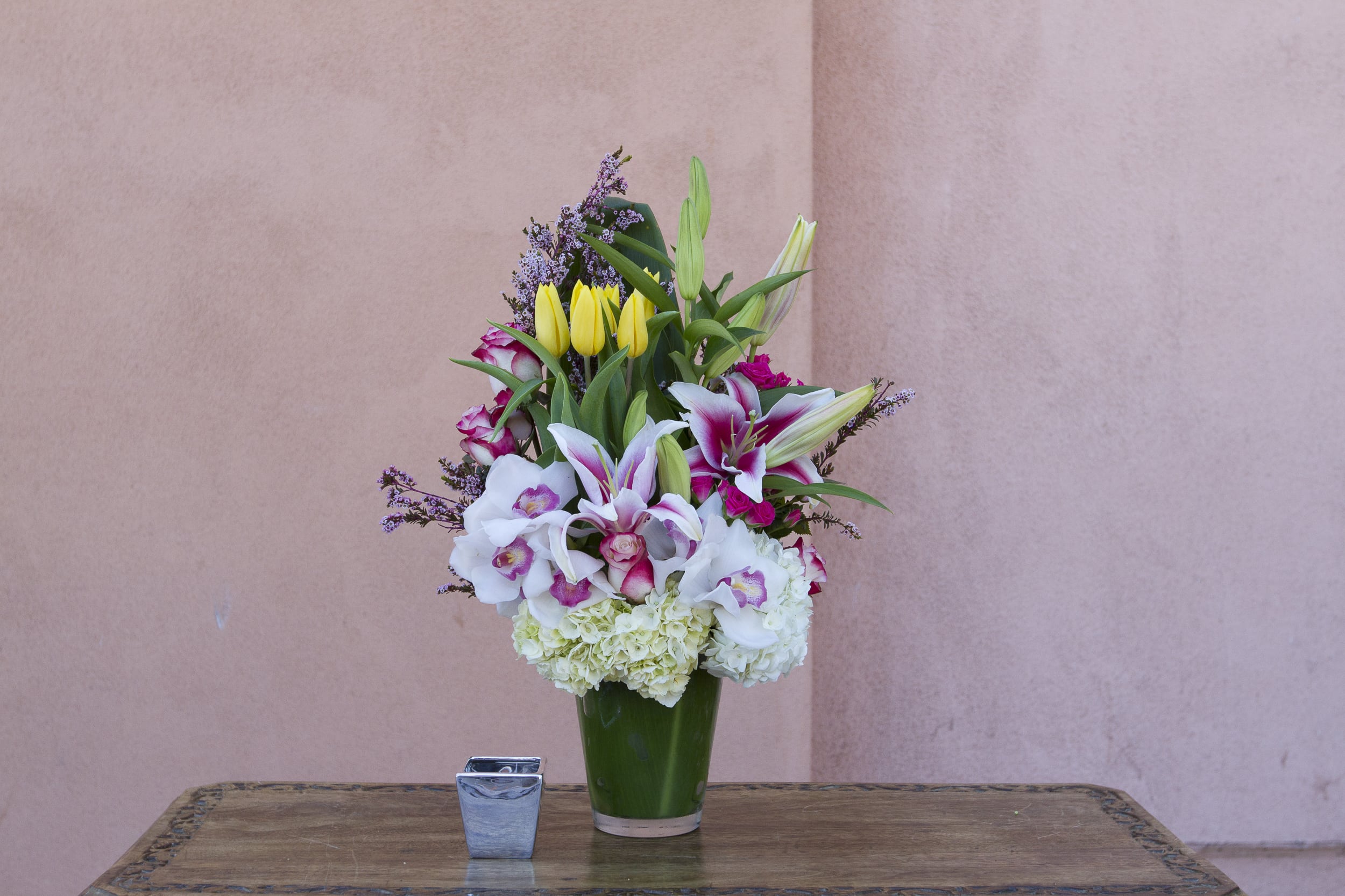 Tall bouquet of lilies, tulips, orchids, and hydrangeas in a green vase