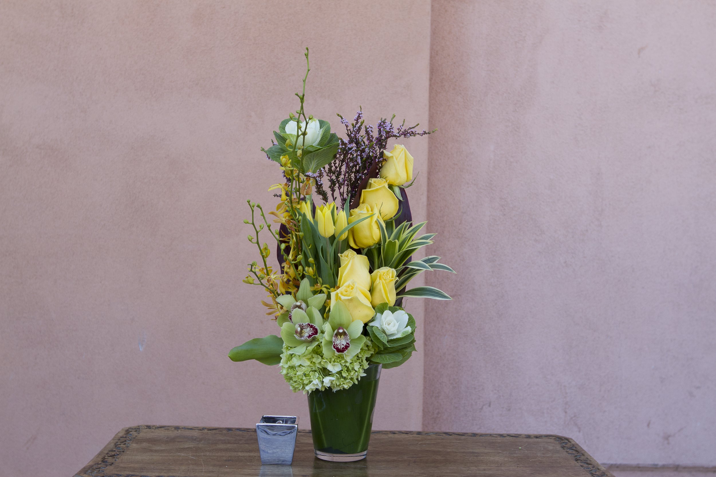 Tall yellow rose arrangement in a green vase with mixed blooms