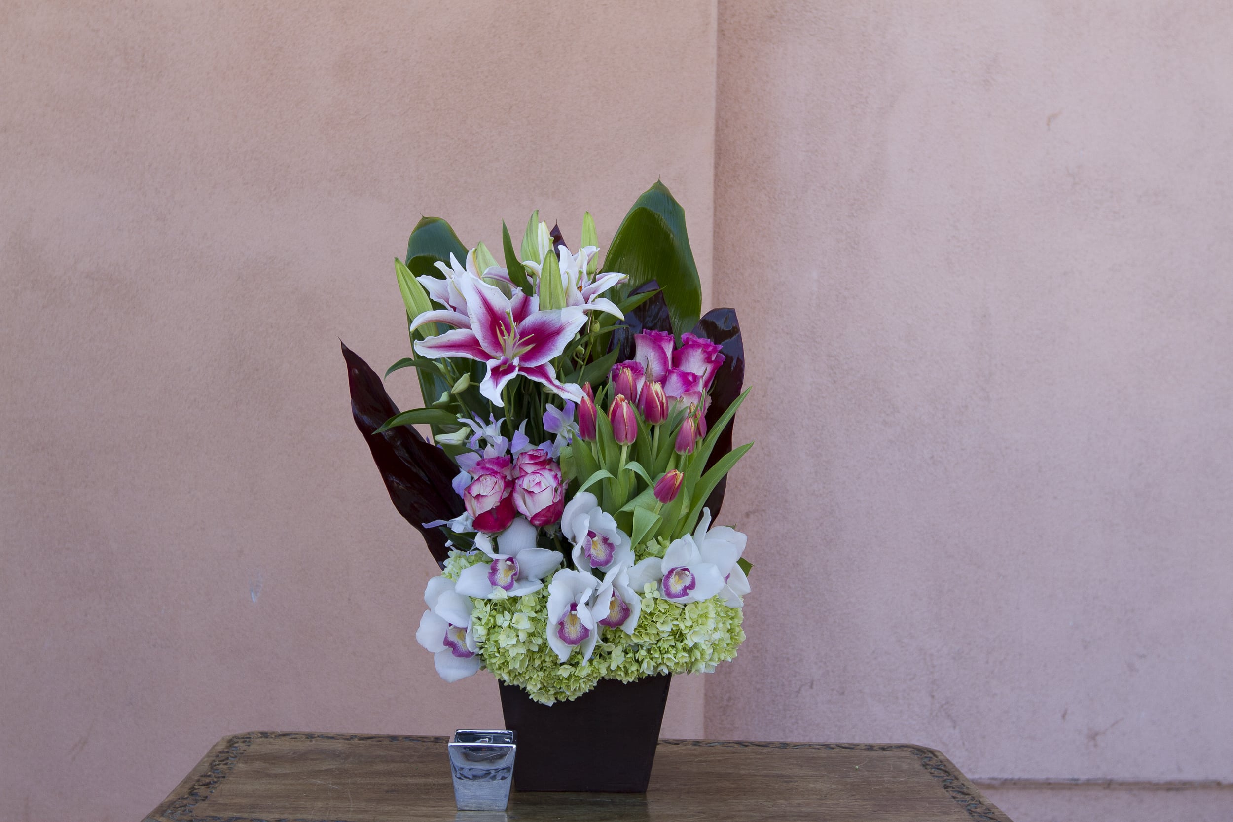Mixed bouquet of lilies, orchids, and roses in a dark vase