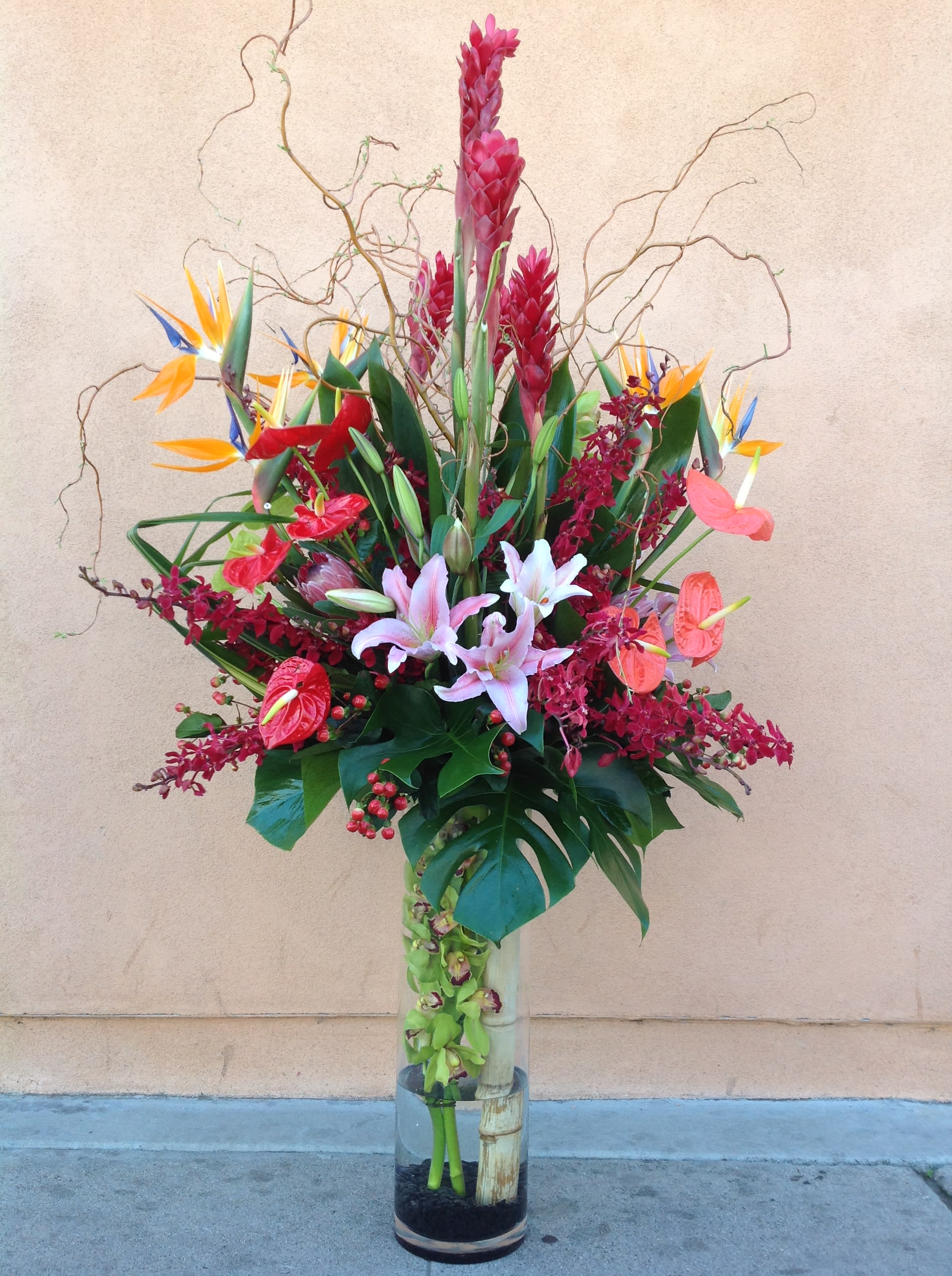 Tall tropical flower arrangement in a clear glass vase with pink lilies and bird of paradise