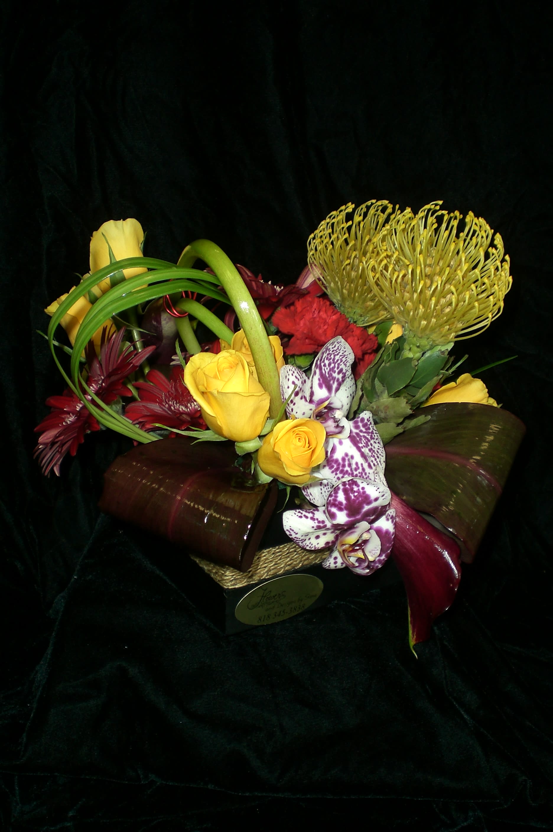 Mixed bouquet with yellow roses, orchids, and red flowers in a low container