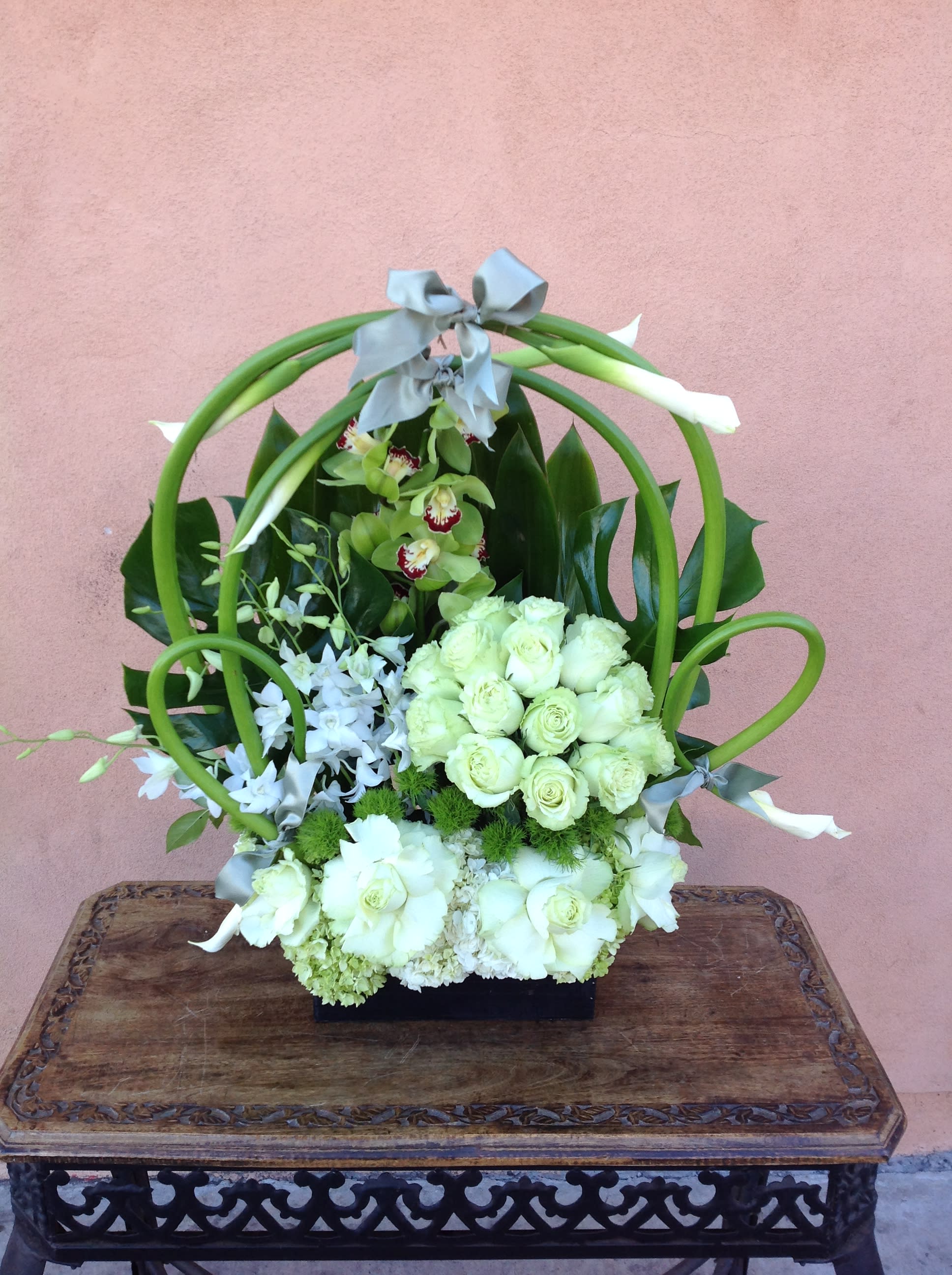 White floral arrangement with green loops and gray ribbon on a black base