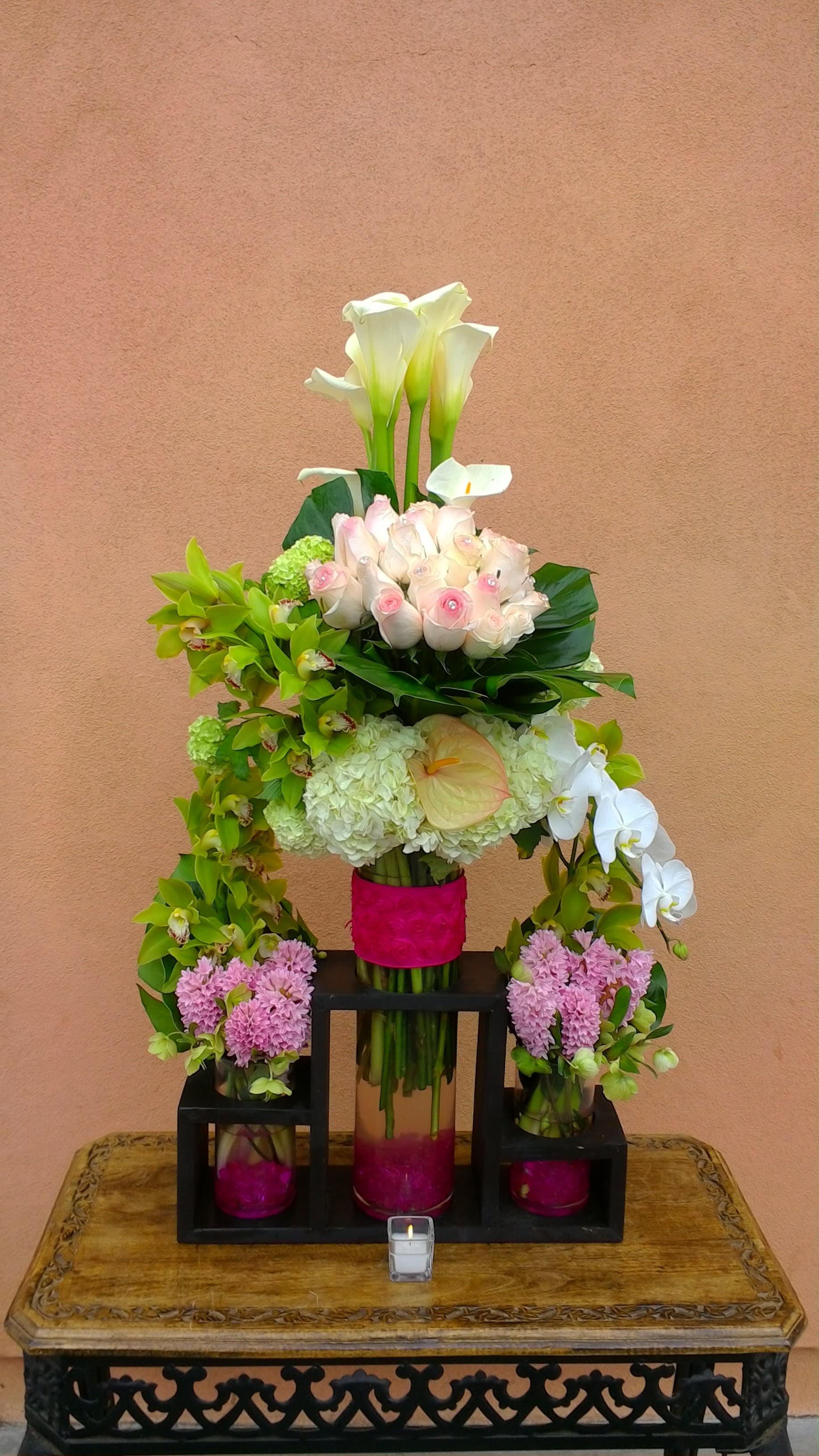 Tiered floral arrangement with white calla lilies, pink roses, and orchids in glass vases