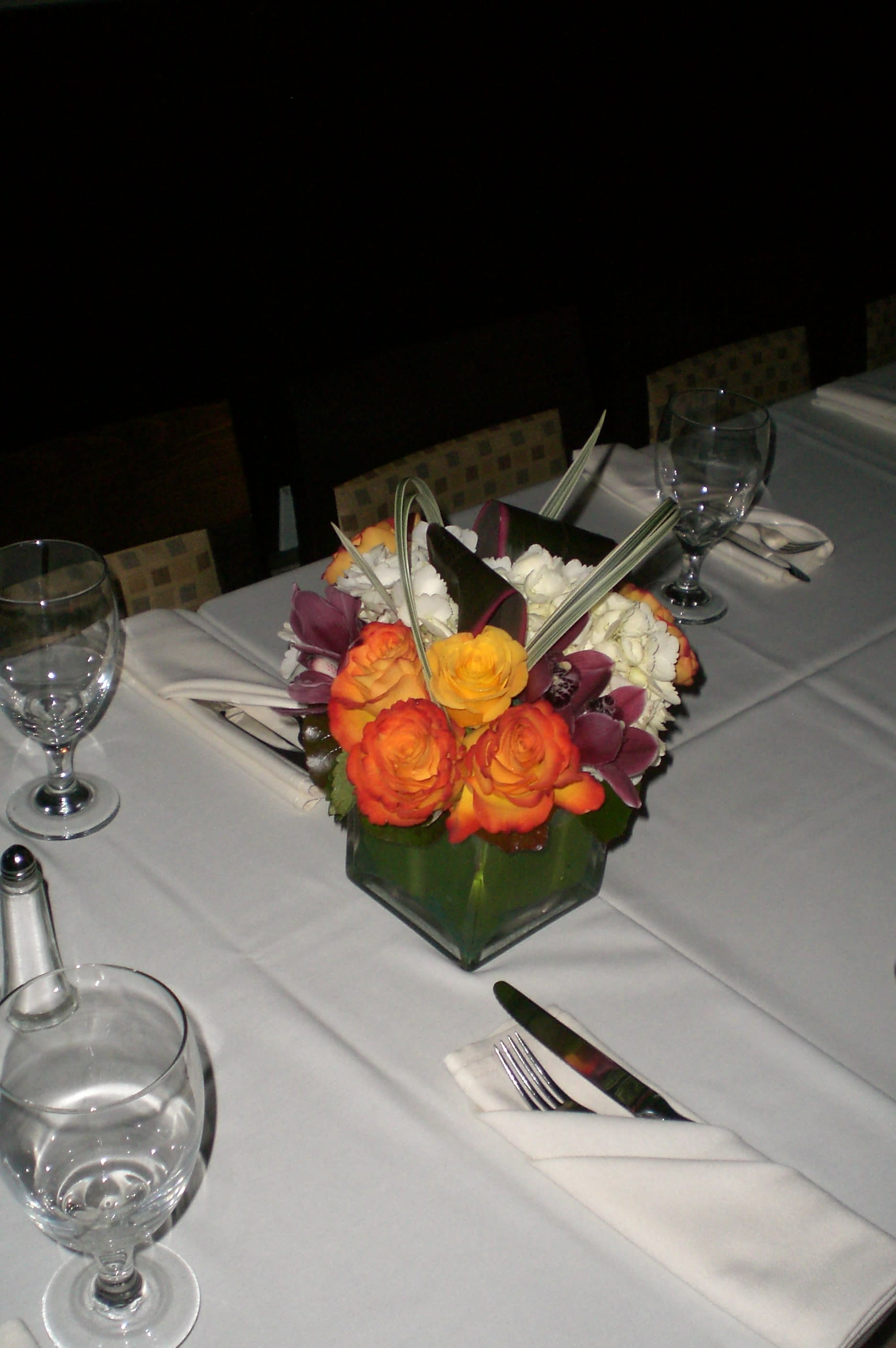 Table centerpiece with orange and purple flowers in a green glass vase
