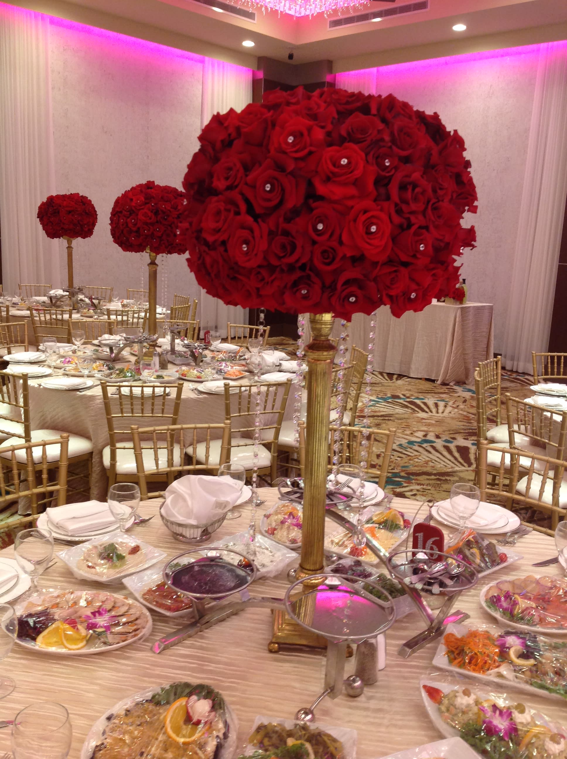 Large red rose centerpiece on a tall gold stand at a banquet table