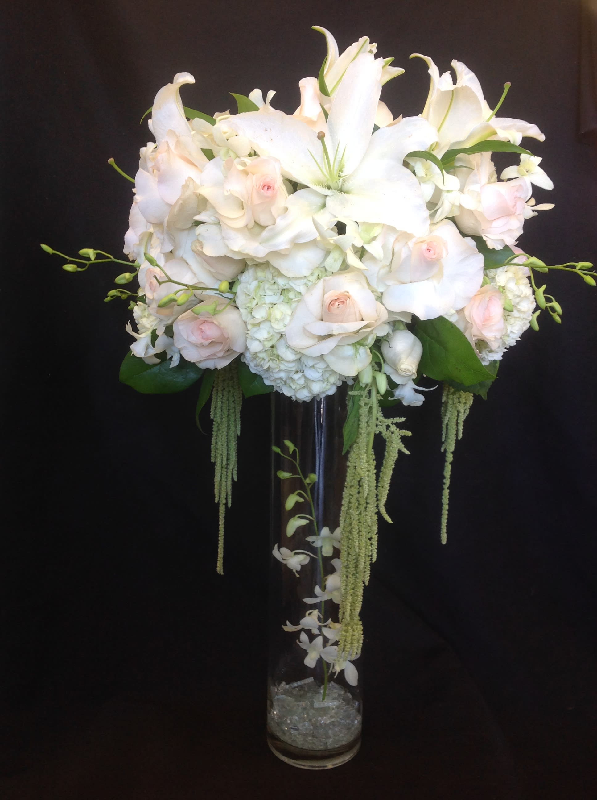 White lilies and pale pink roses in a tall glass vase