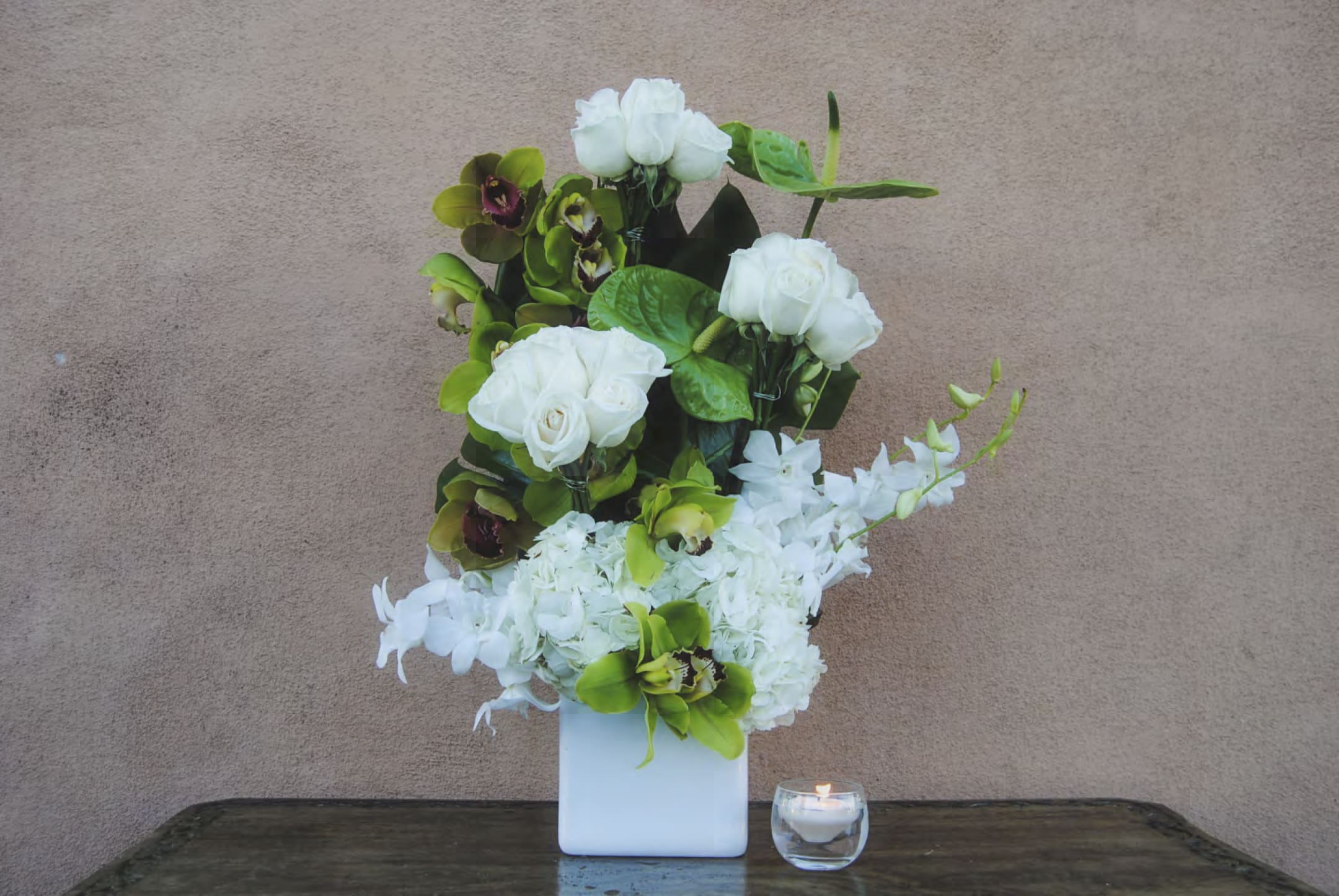 White floral arrangement in a square vase with a small candle beside it