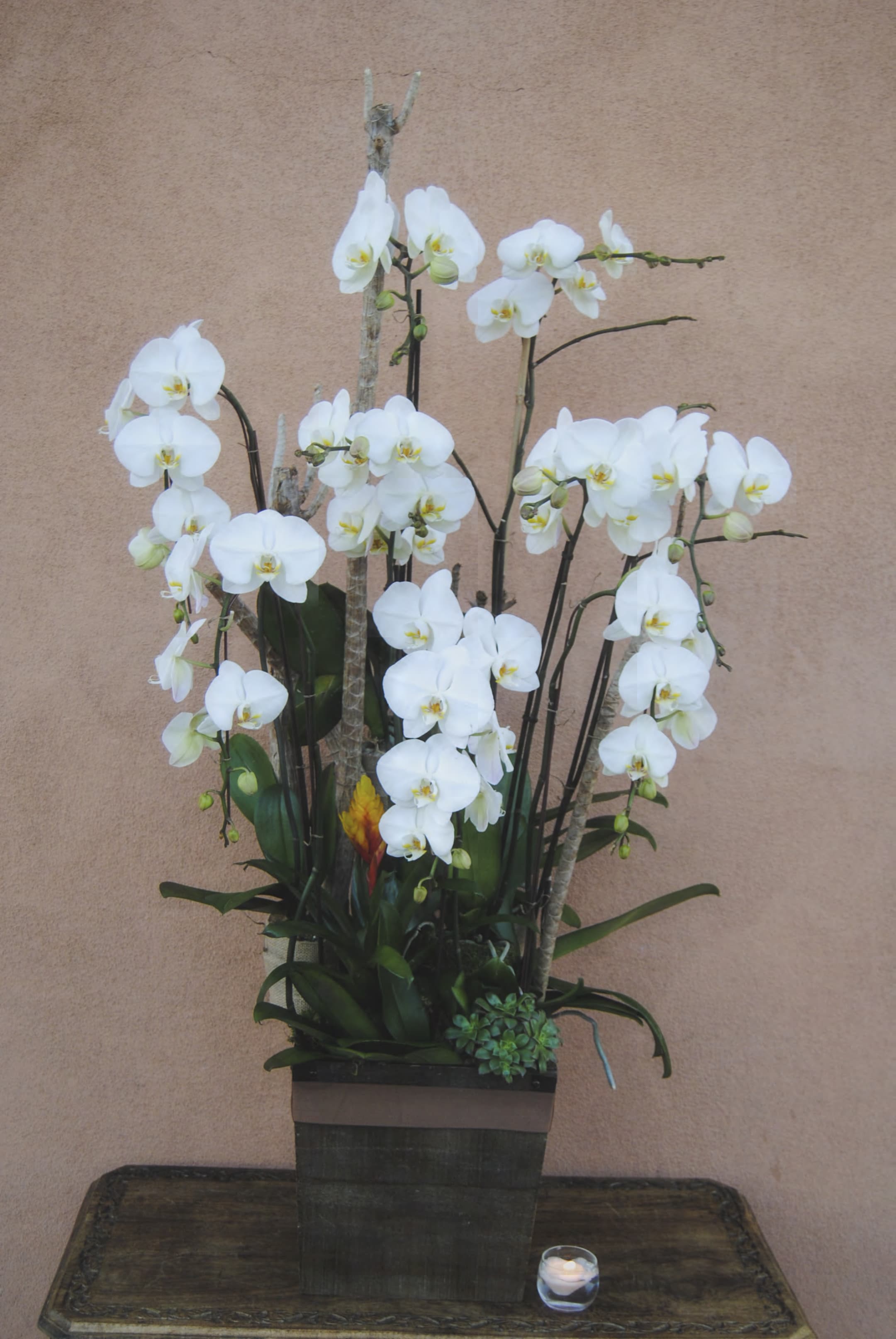 White orchid arrangement in a square planter with a small candle beside it