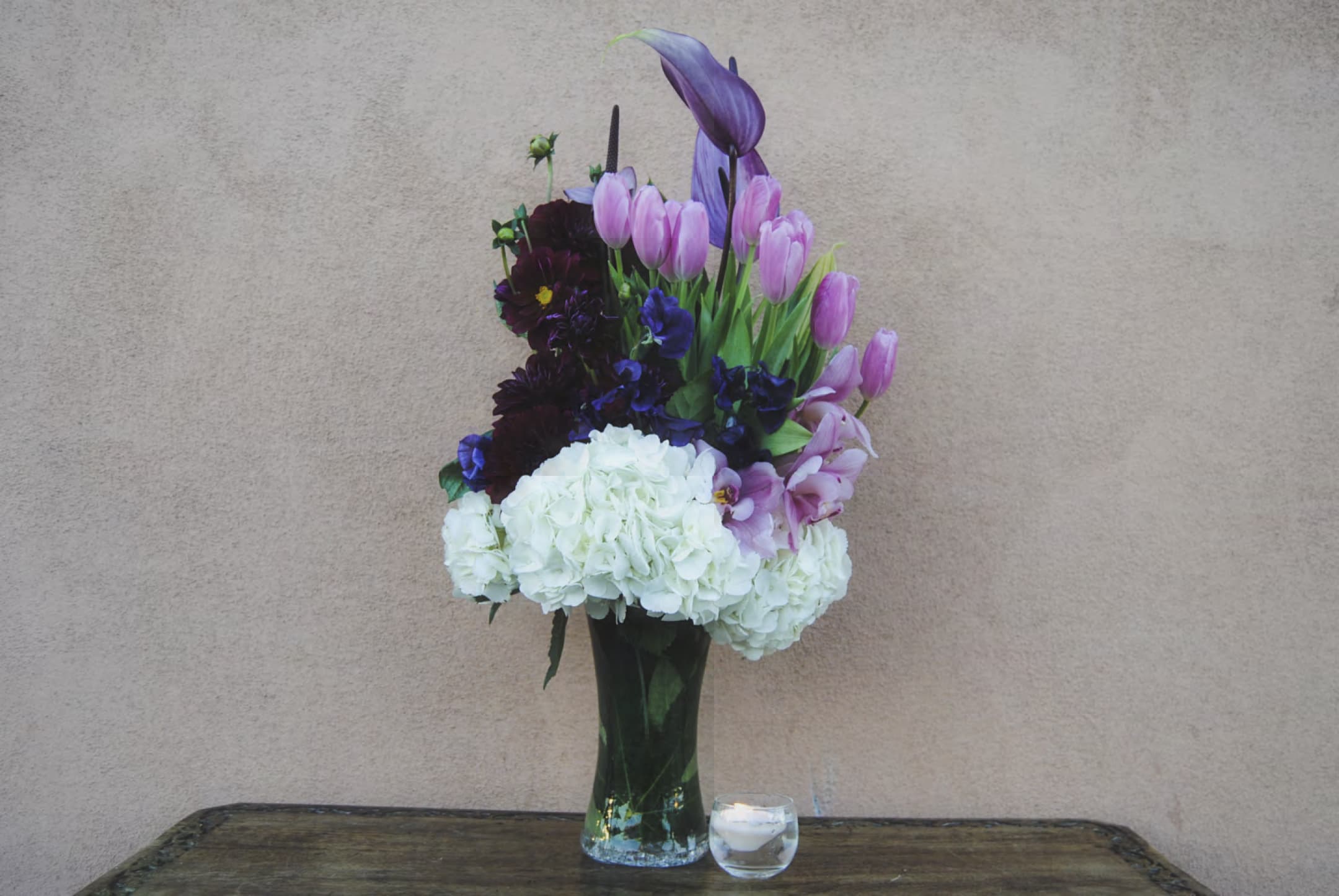 Tall bouquet of pink tulips, purple flowers, and white hydrangeas in a glass vase