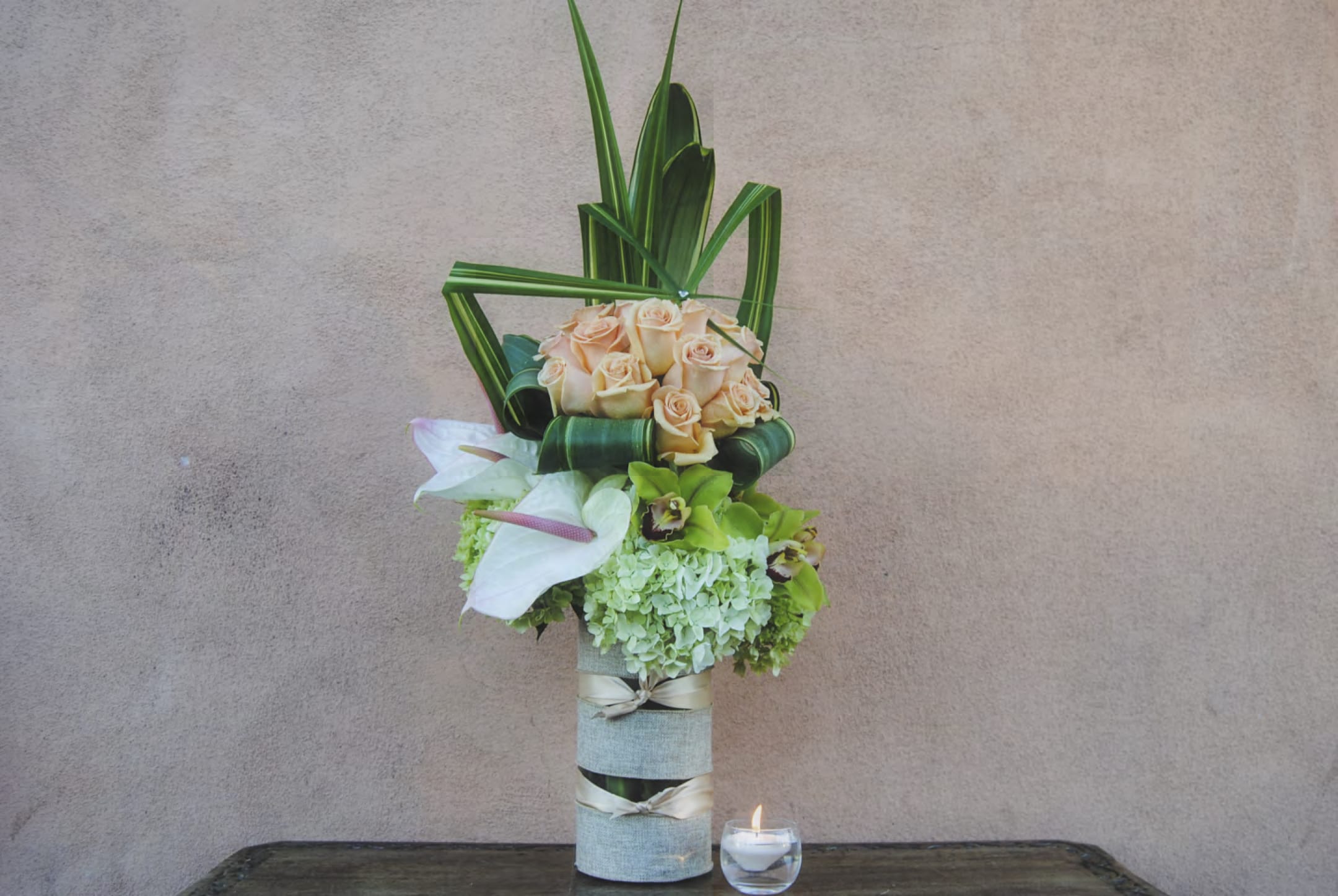 Tall floral arrangement with peach roses and white calla lilies in a wrapped vase