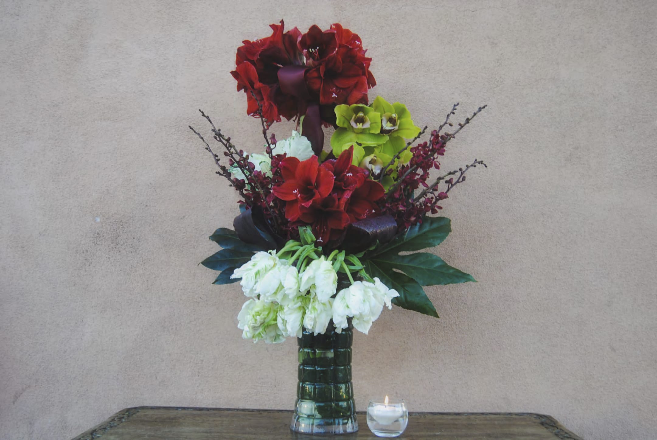 Tall floral arrangement with red, green, and white blooms in a glass vase