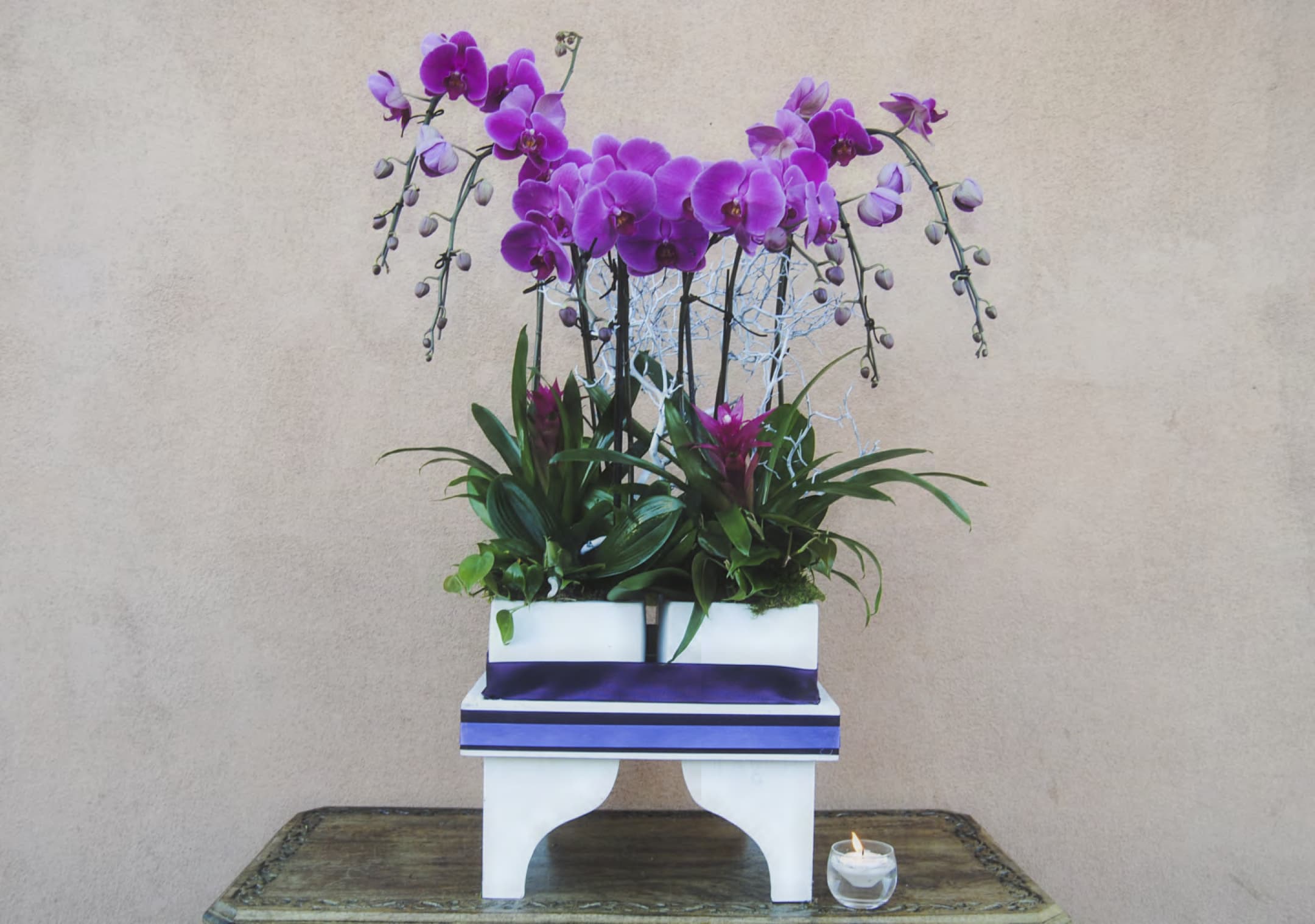 Purple orchid arrangement in a white container with a small candle beside it
