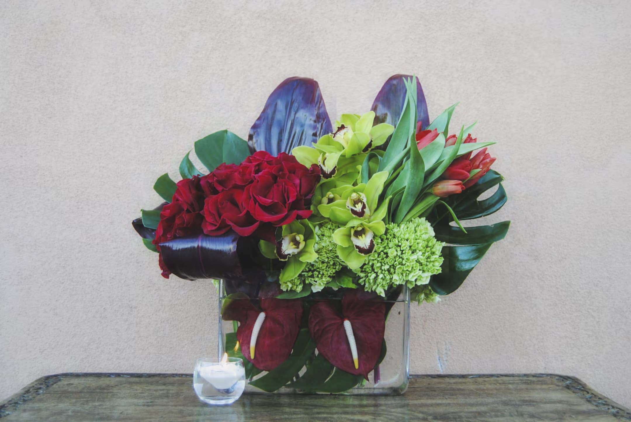 Red roses and green orchids arranged in a clear square vase