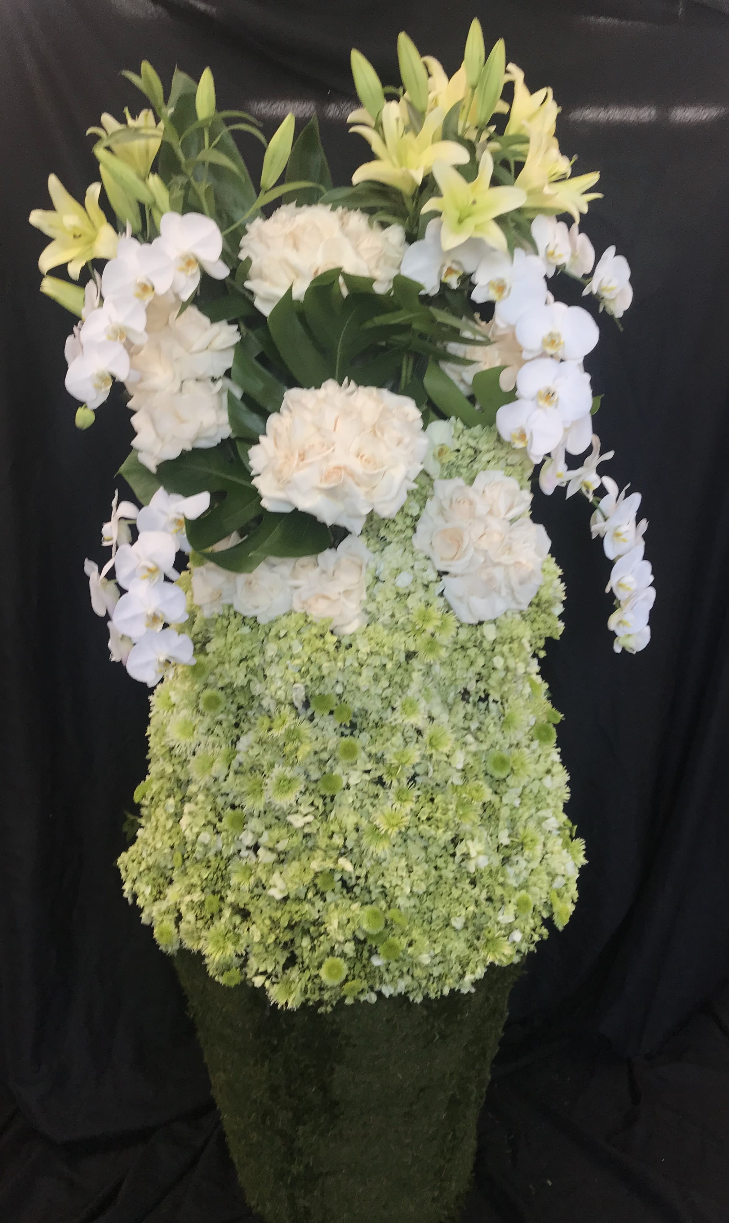 Tall floral arrangement with white orchids, lilies, roses, and green blooms