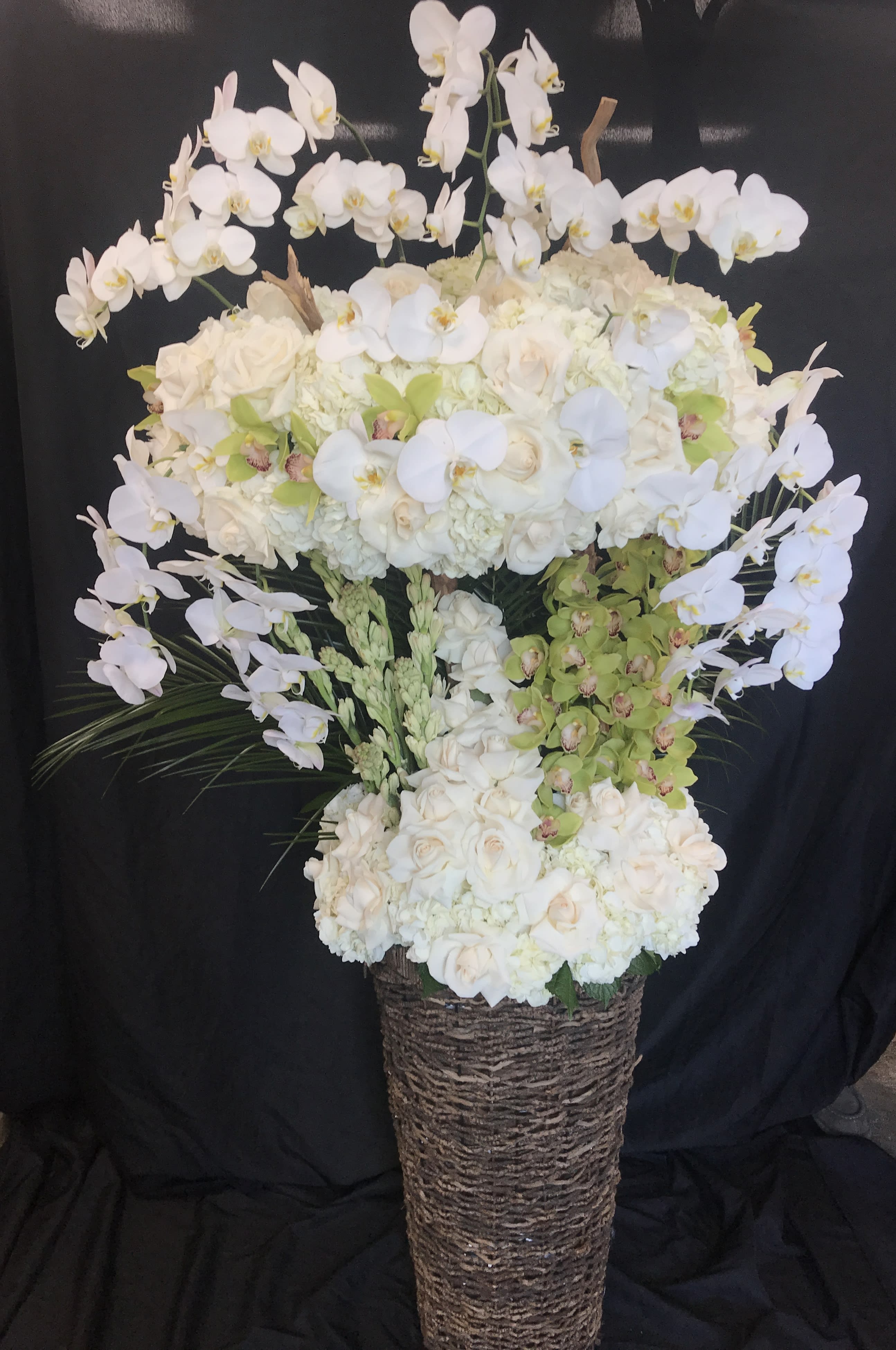 Tall white floral arrangement in a woven basket with arching orchids