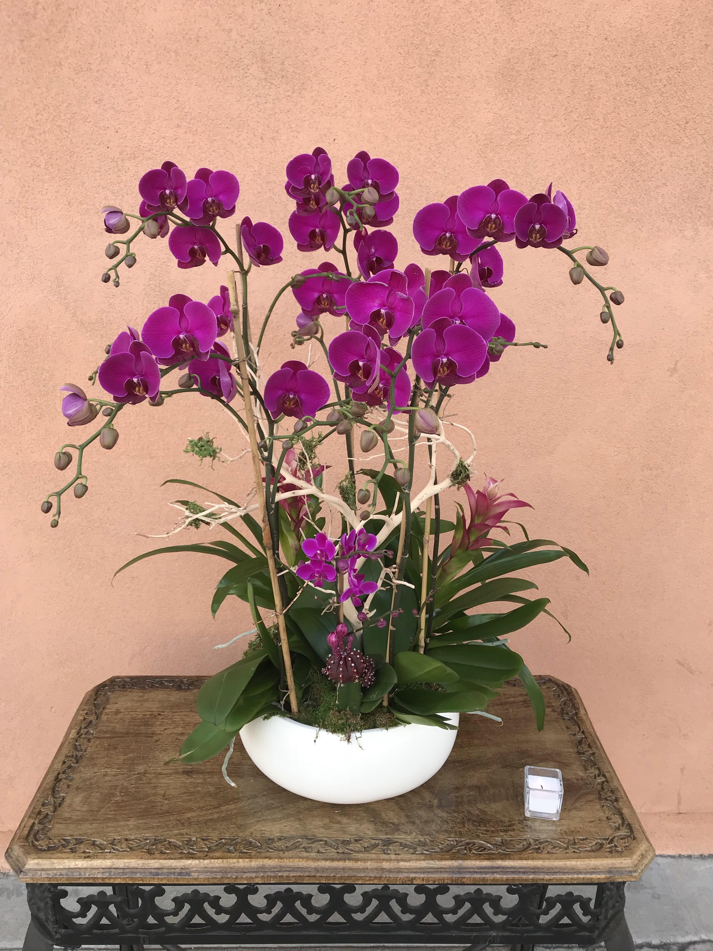 Purple orchid arrangement in a white bowl vase on a wooden table