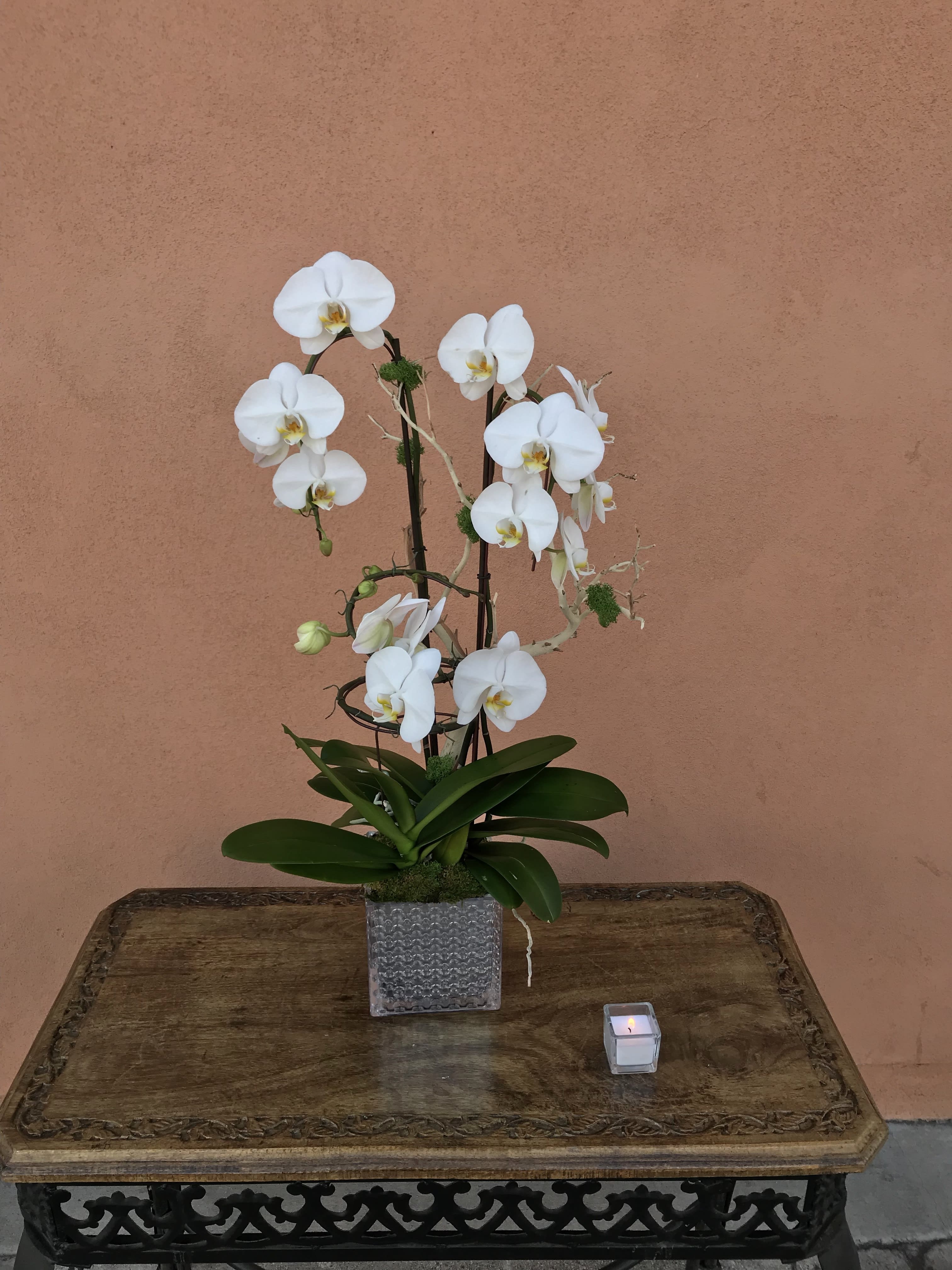 White orchid arrangement in a square glass vase with a small candle beside it