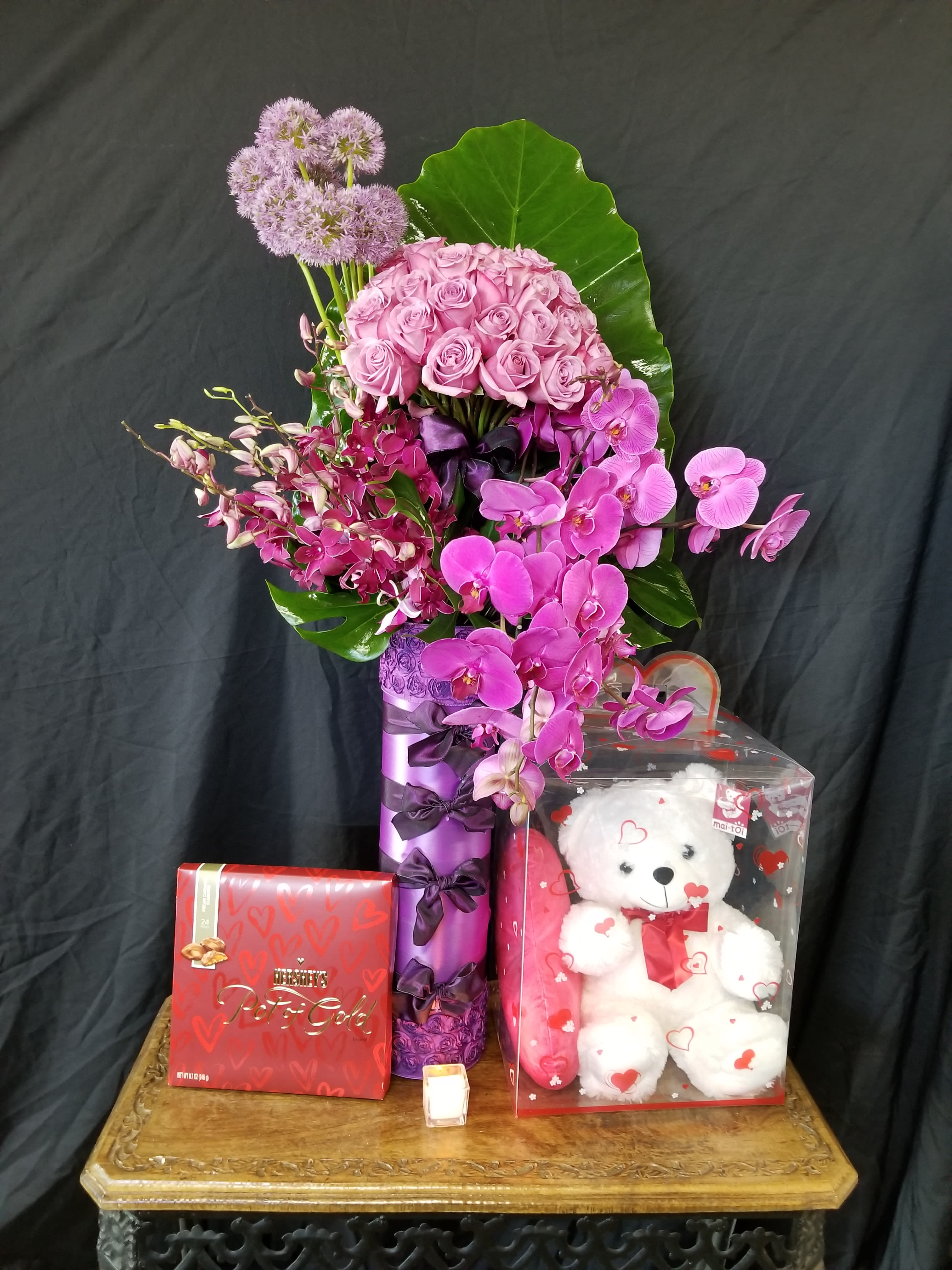 Pink roses and orchids arranged with a teddy bear and chocolates