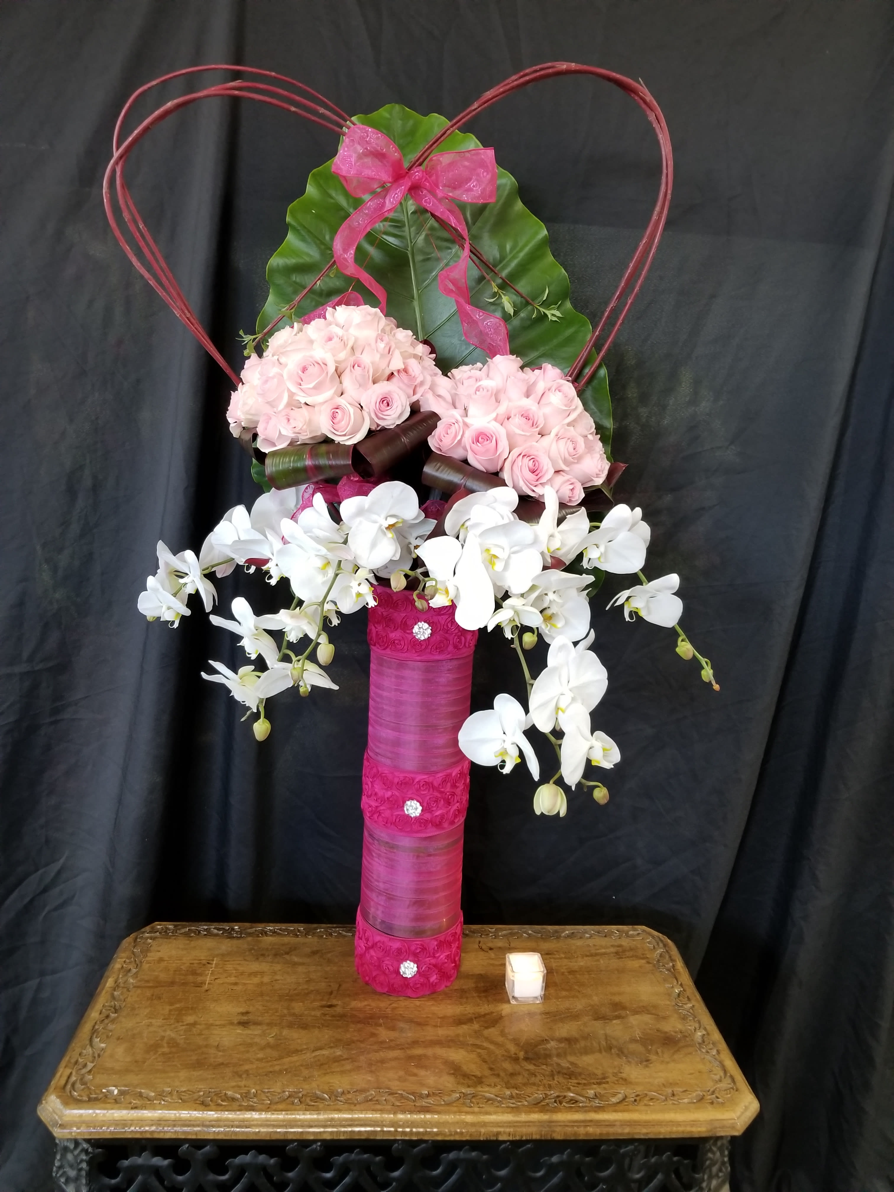 Pink roses and white orchids arranged in a tall decorative vase with a heart frame