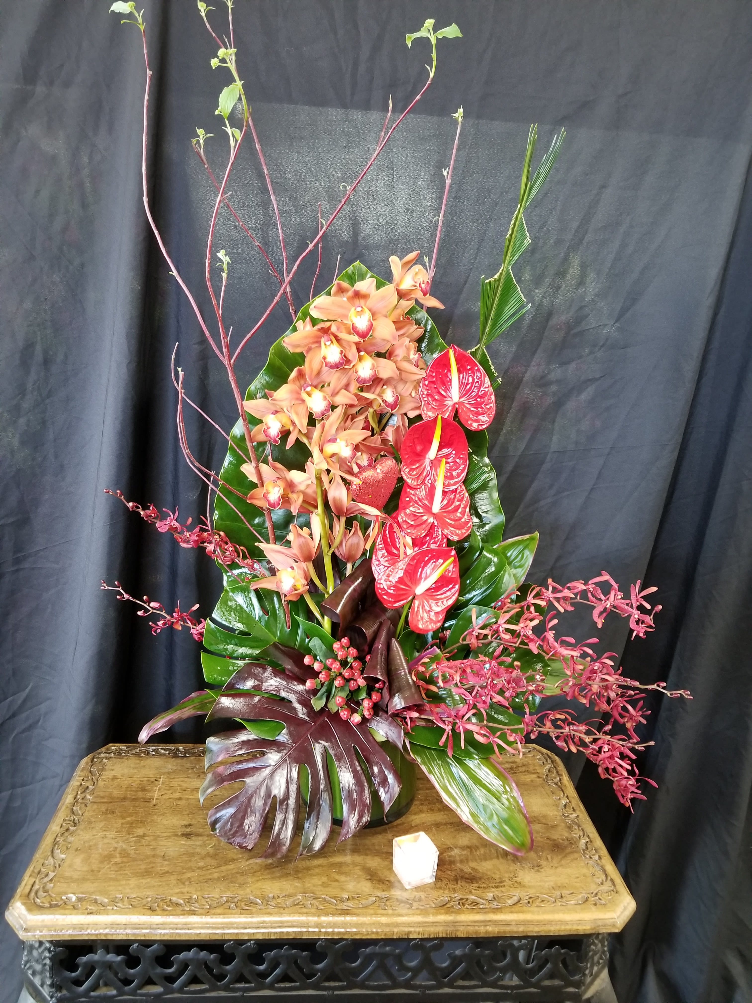 Tall tropical arrangement with orchids and red anthuriums in a vase