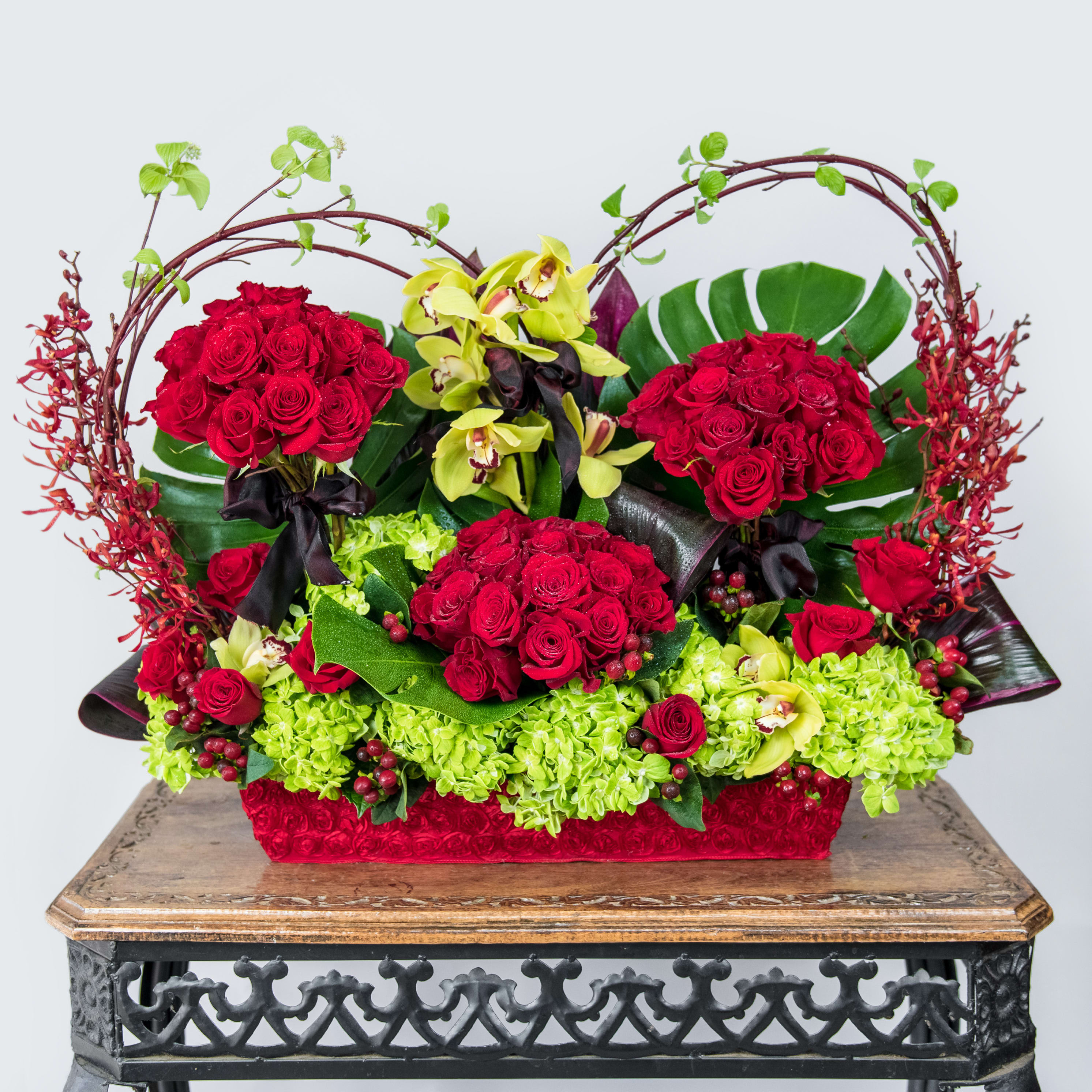 Red roses and green orchids in a decorative basket arrangement