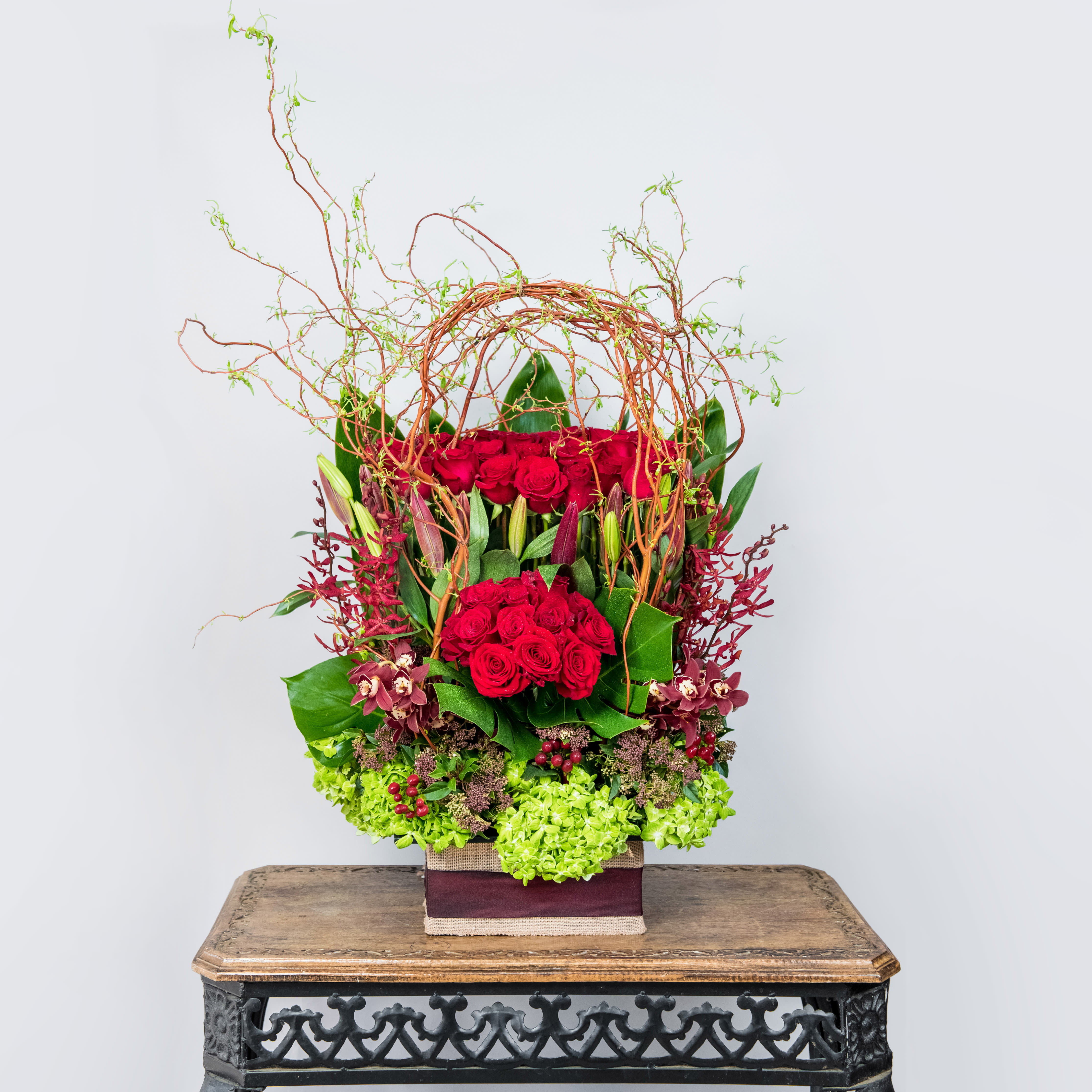 Tall arrangement of red roses with green accents in a square container