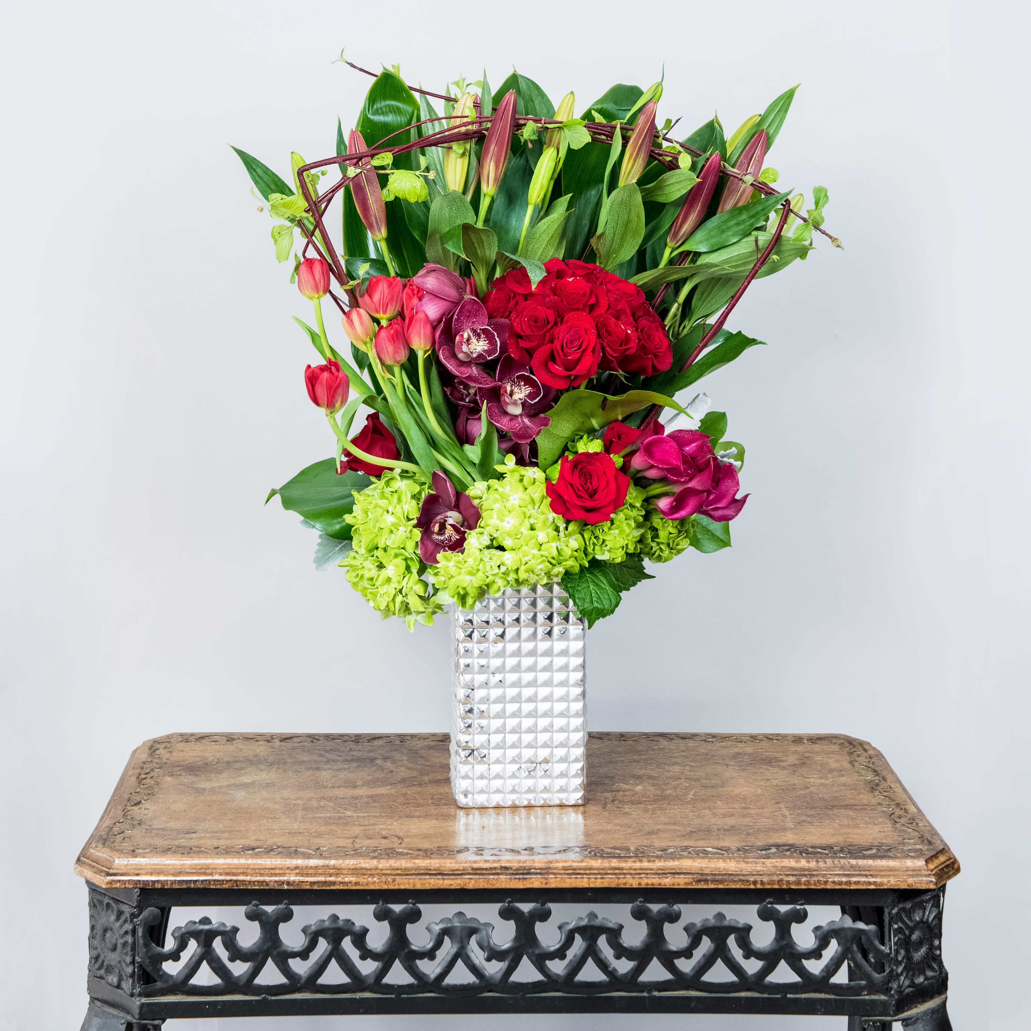 Bouquet of red roses, orchids, and tulips in a silver vase