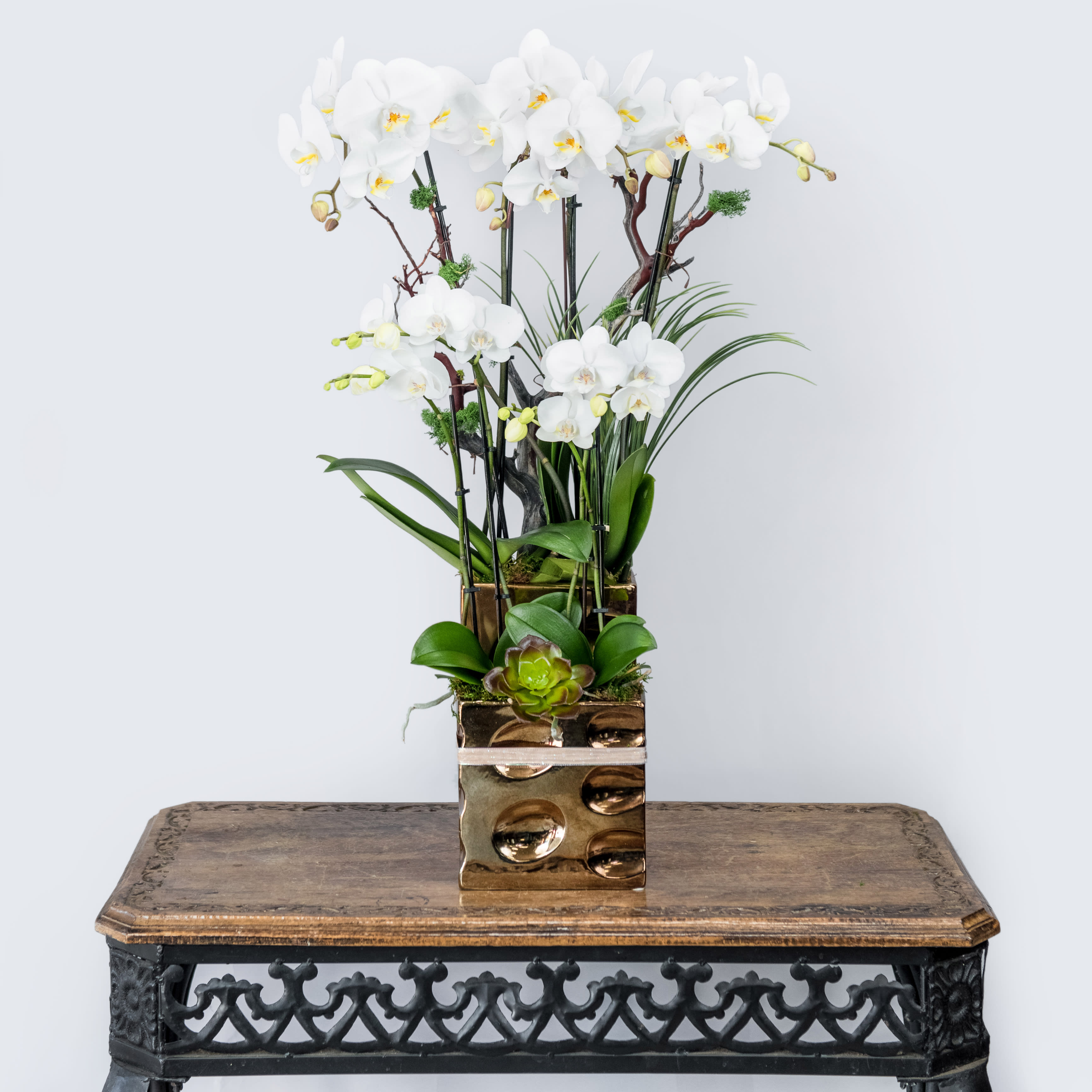 Tall arrangement of white orchids in a gold square vase