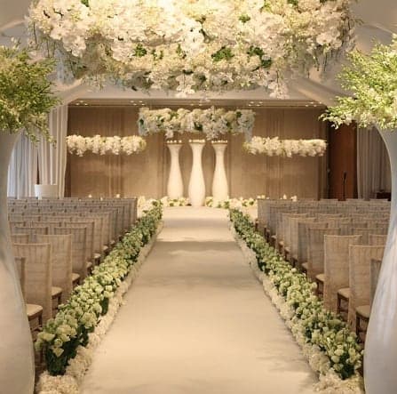 White floral wedding aisle with hanging arrangements and tall pedestal centerpieces