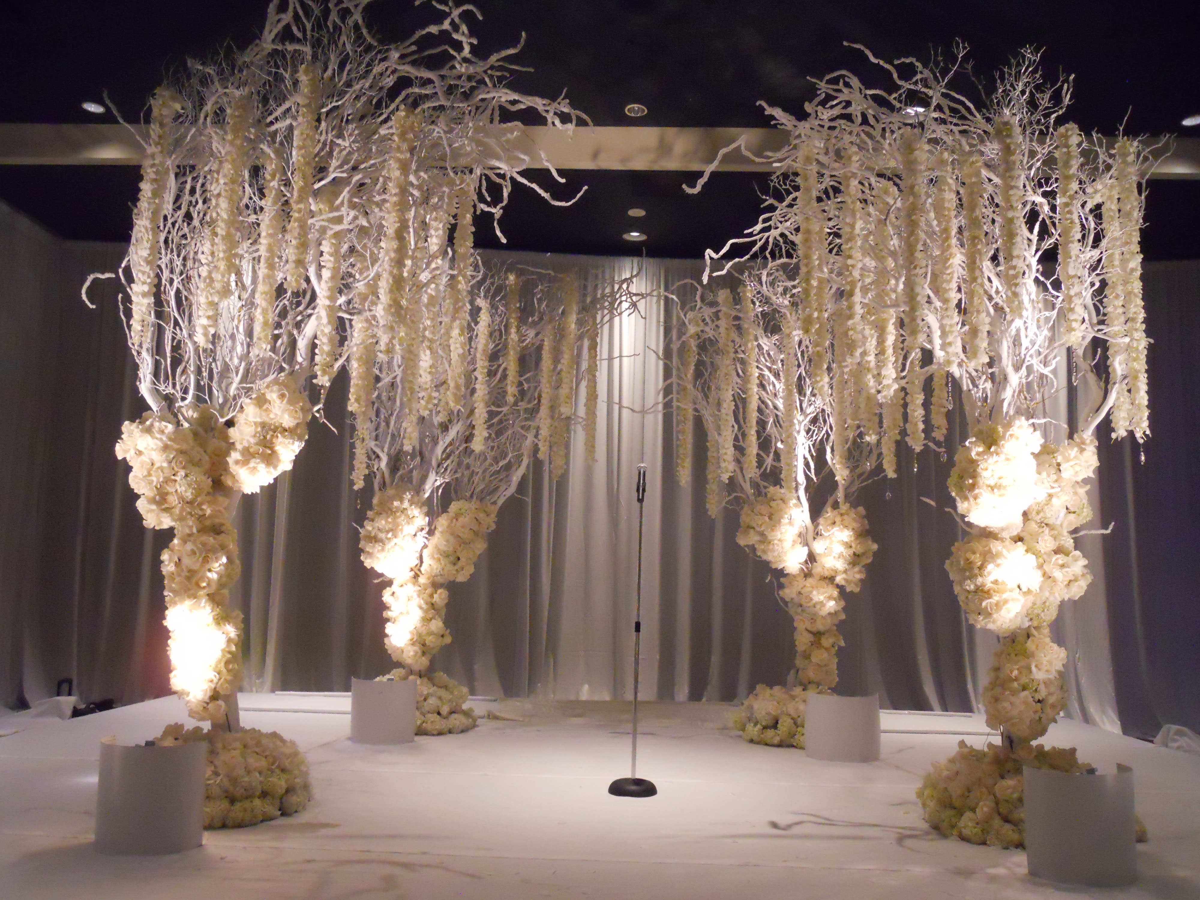 Tall white floral installations frame a stage with a microphone stand