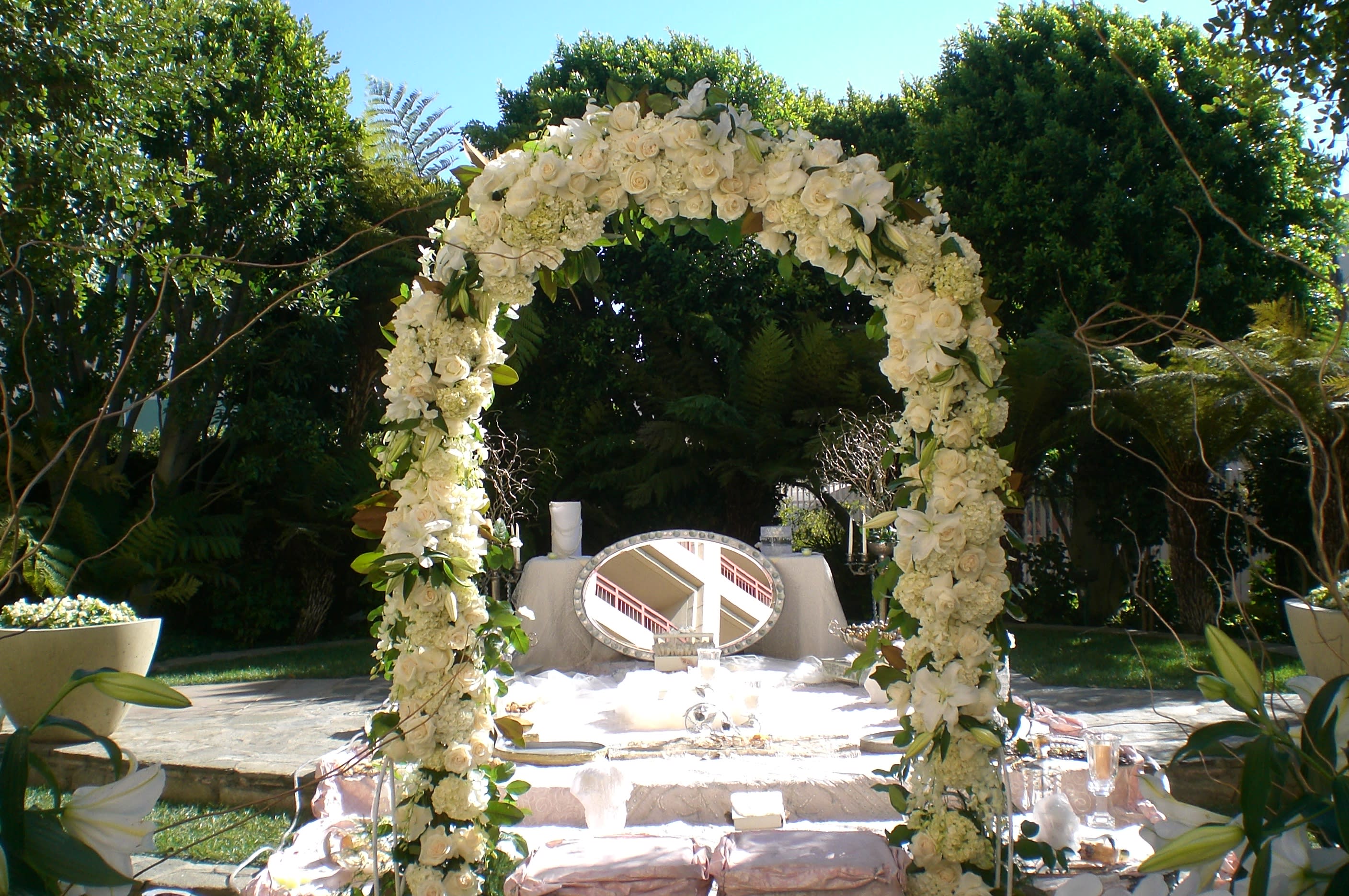 White floral arch over an outdoor ceremony table with candles and a mirror