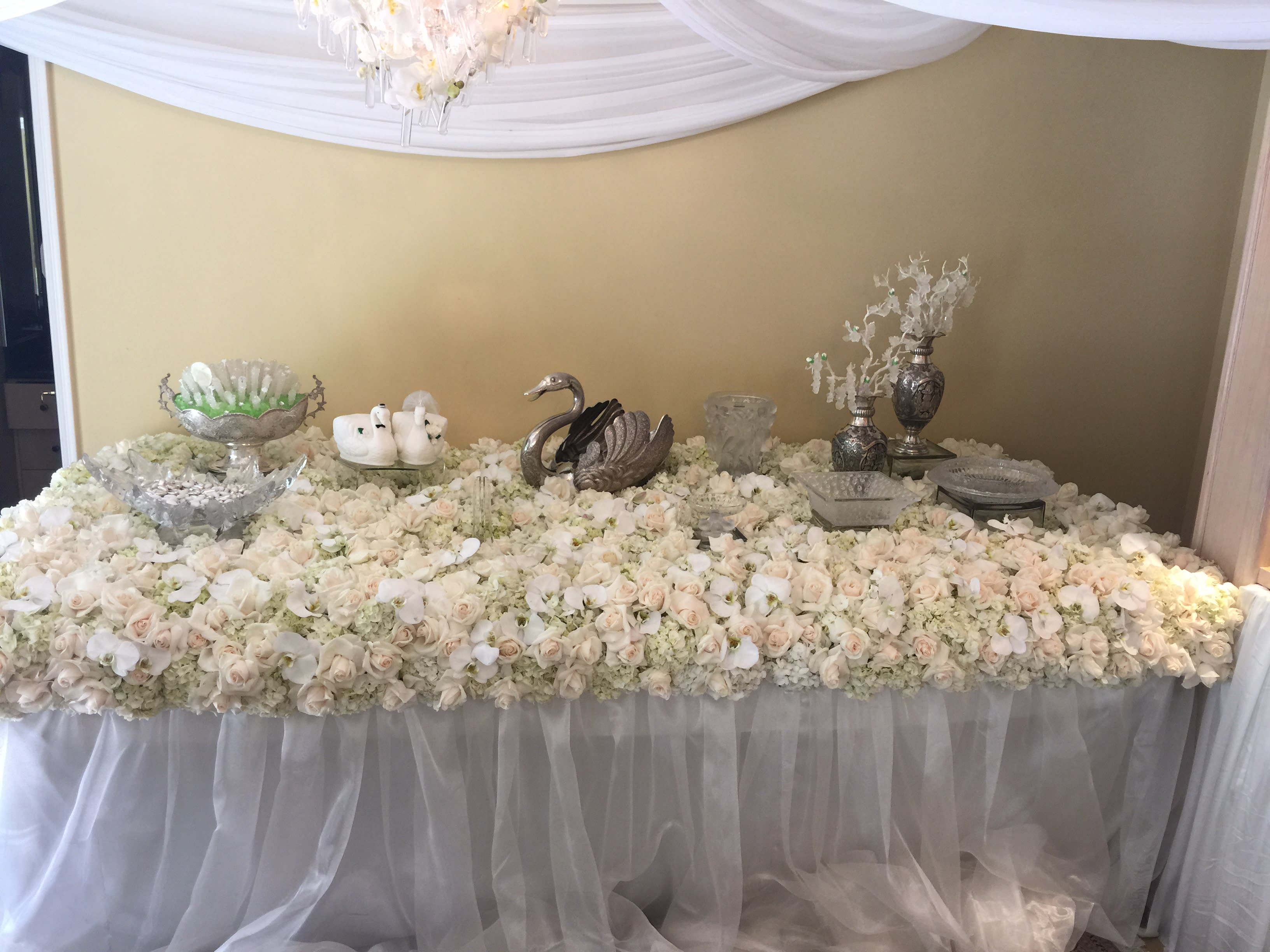 Large table covered in white and blush roses with silver decor pieces