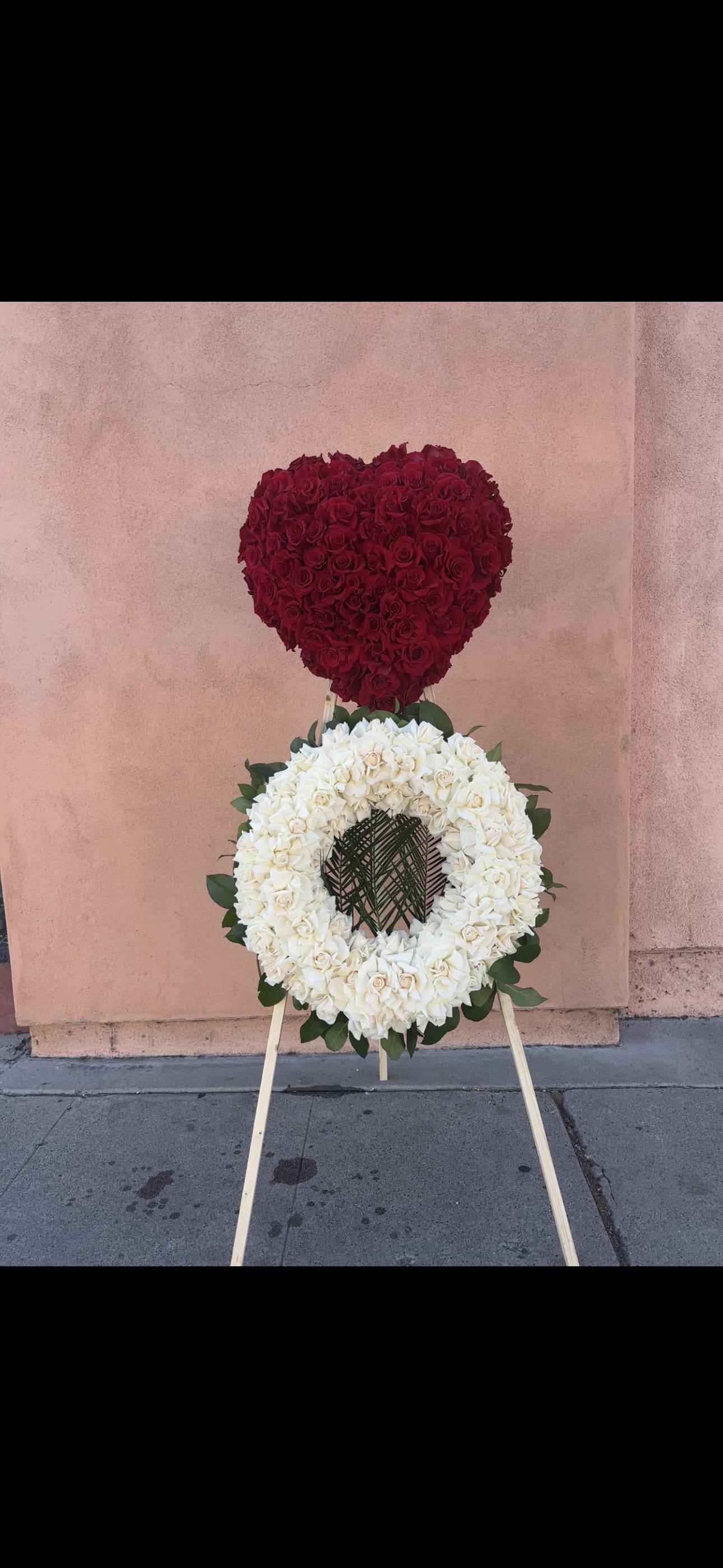 Heart-shaped red rose arrangement above a white rose wreath on an easel