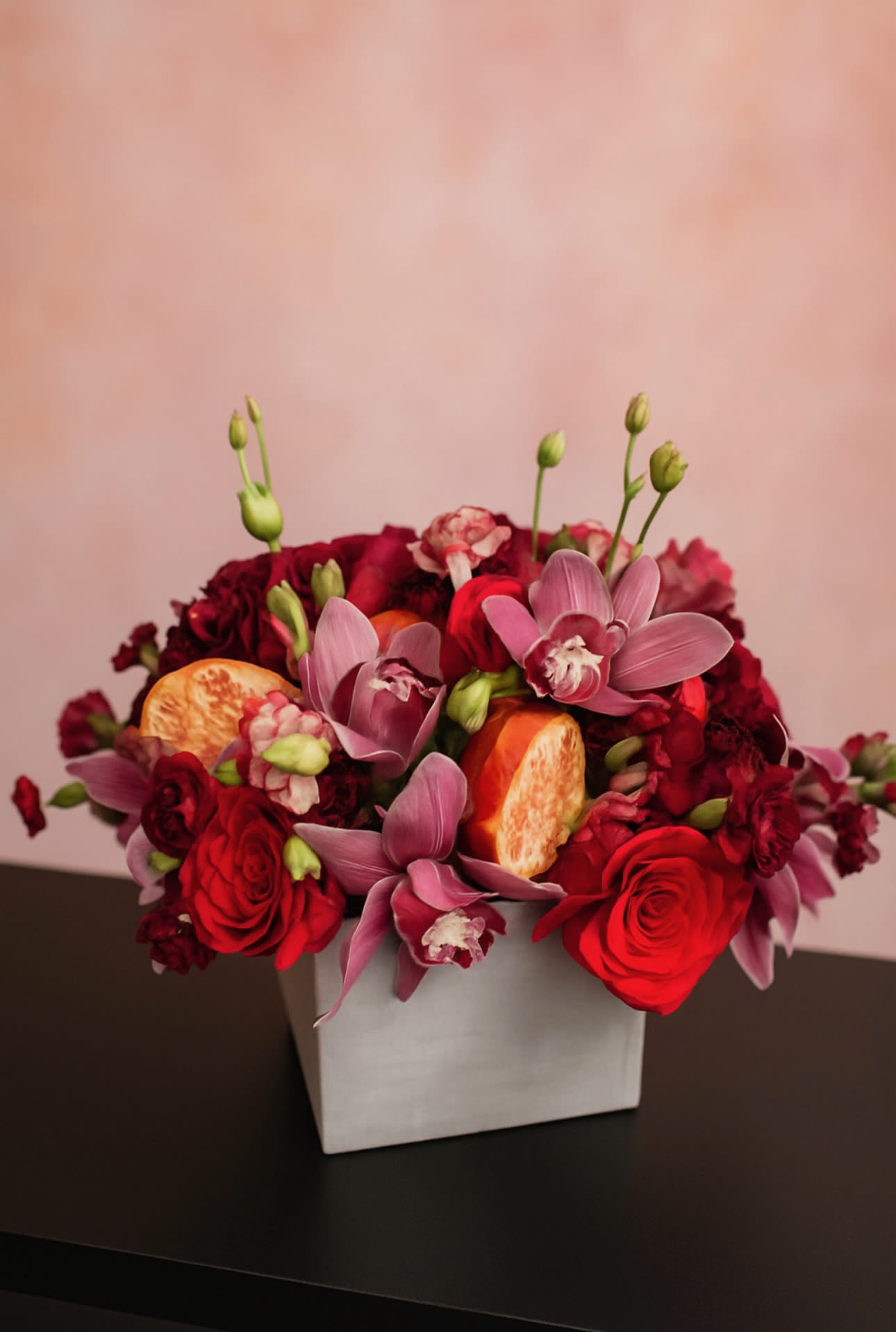 Red and pink floral arrangement in a white square vase