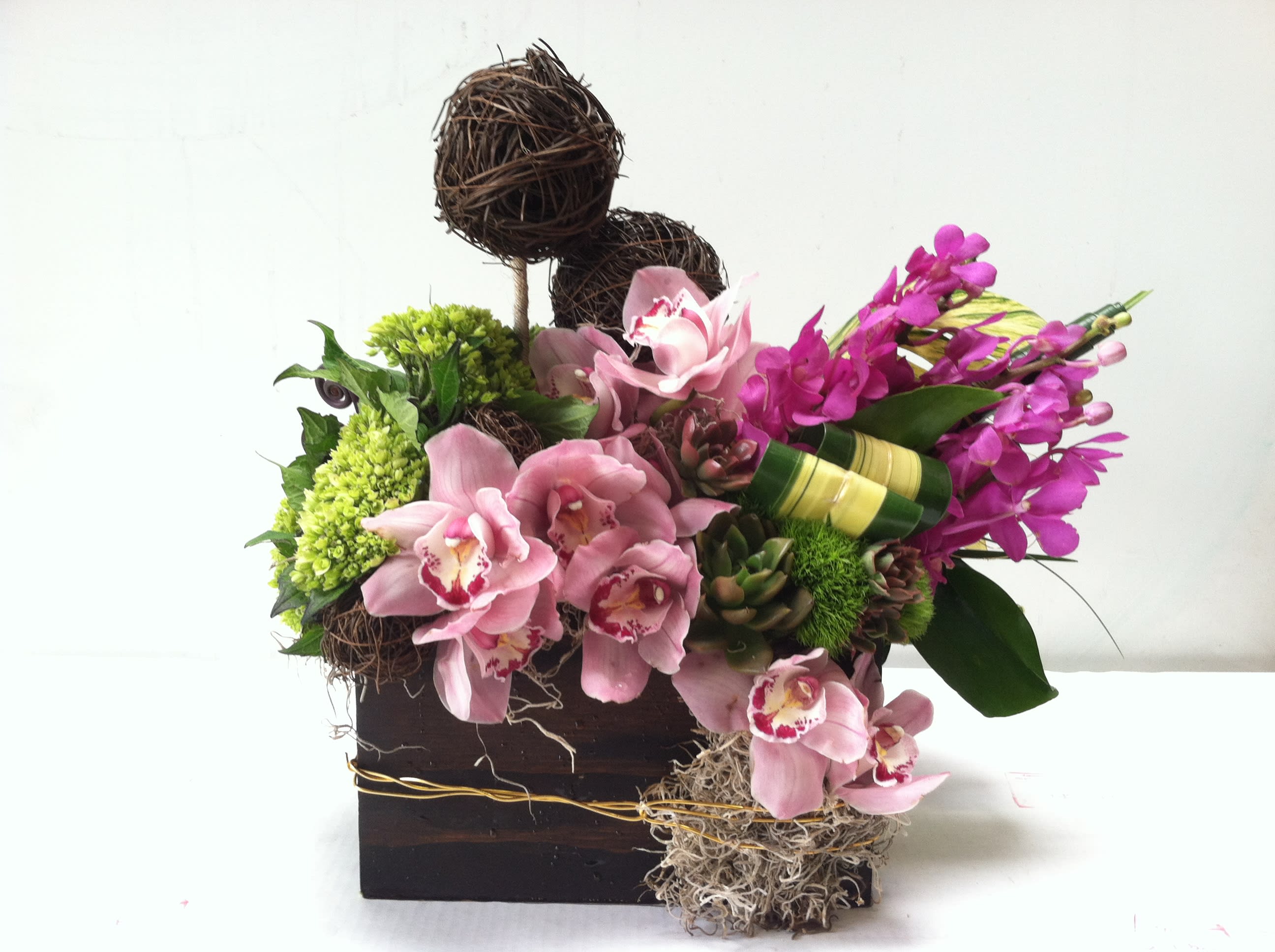 Pink orchids and green blooms arranged in a dark wooden box