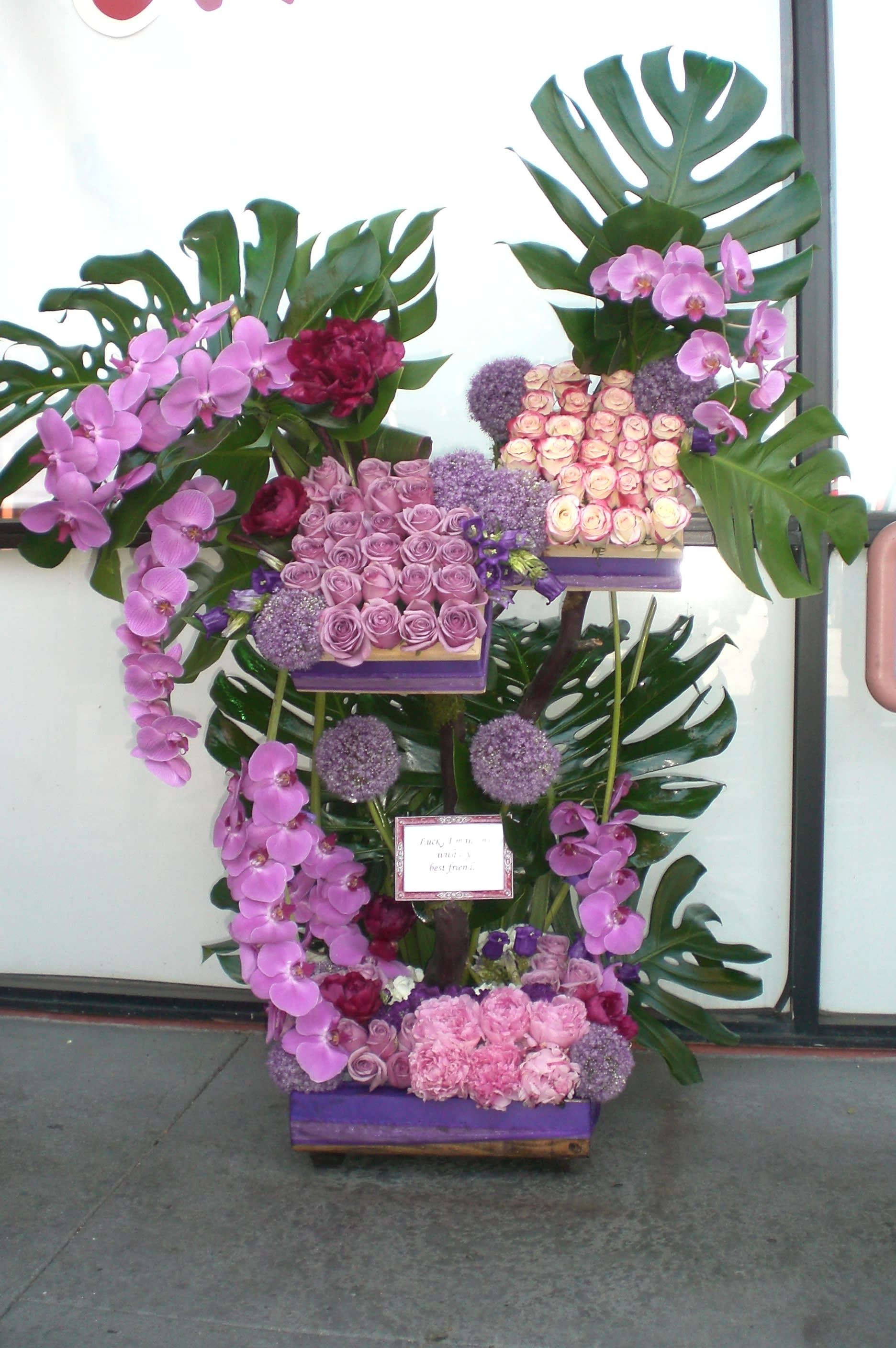 Tall floral display with pink orchids, roses, and large tropical leaves