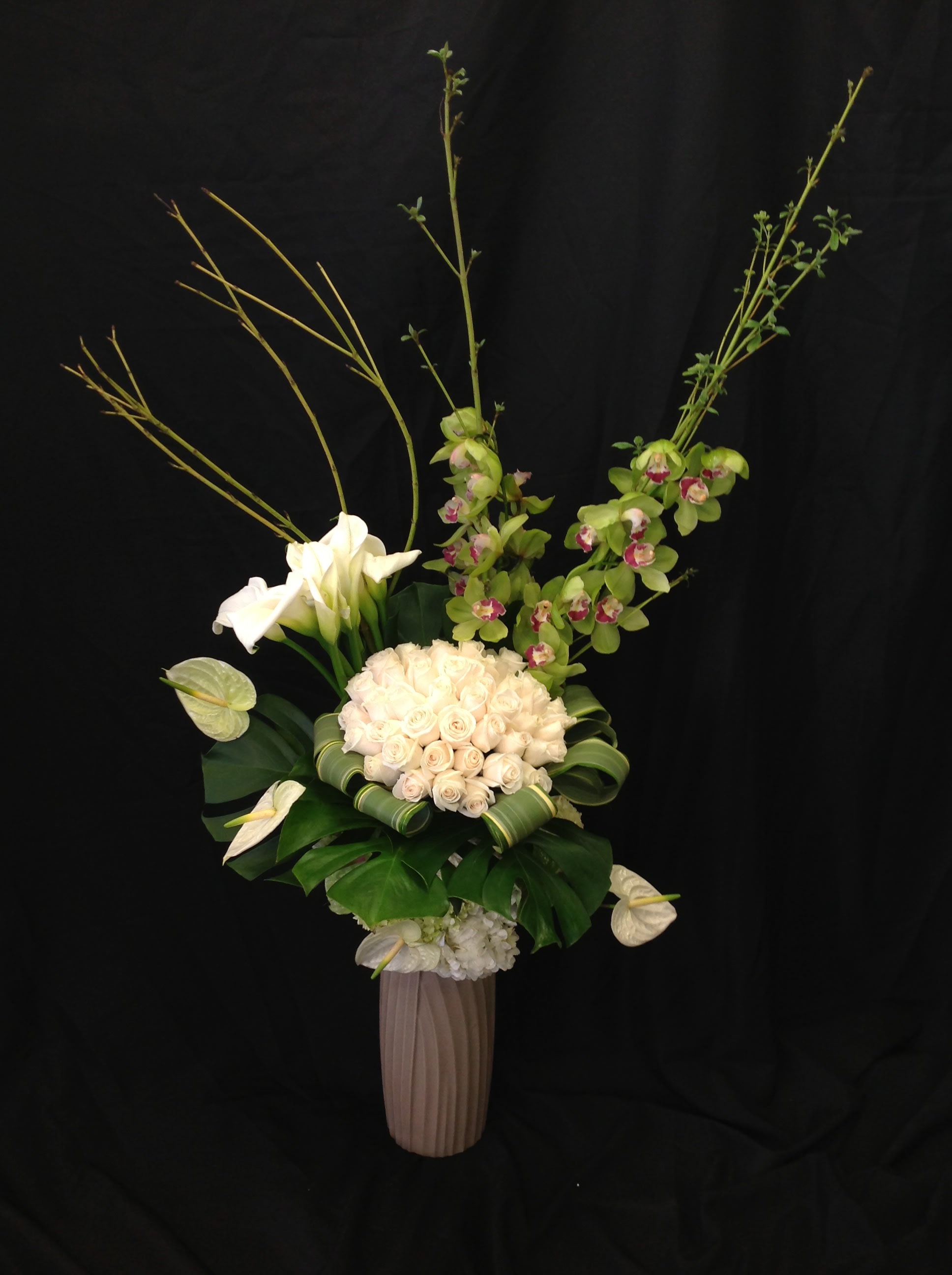 Tall floral arrangement with white roses, calla lilies, and green orchids in a vase