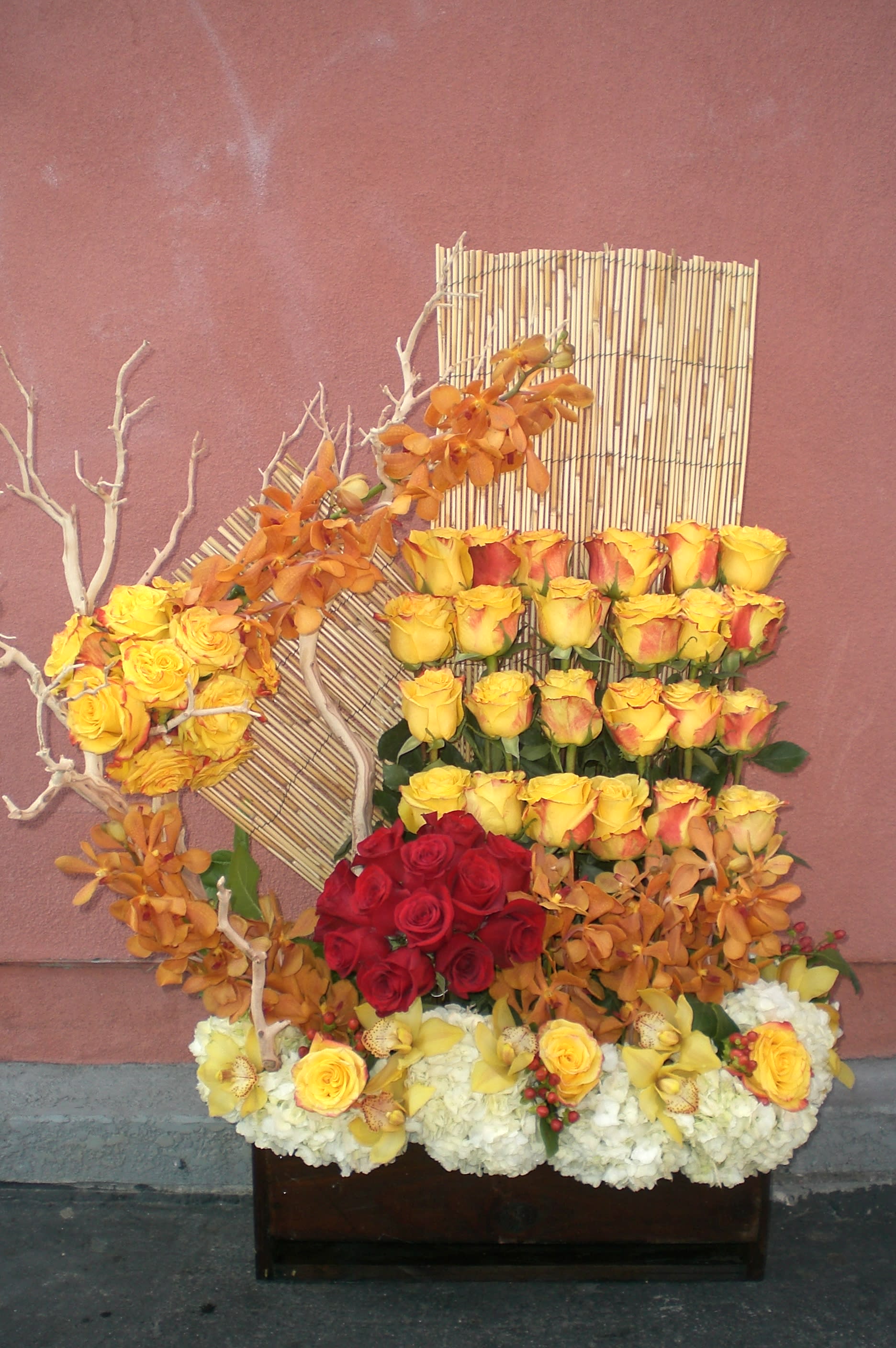 Large floral arrangement with yellow and red roses and orange orchids