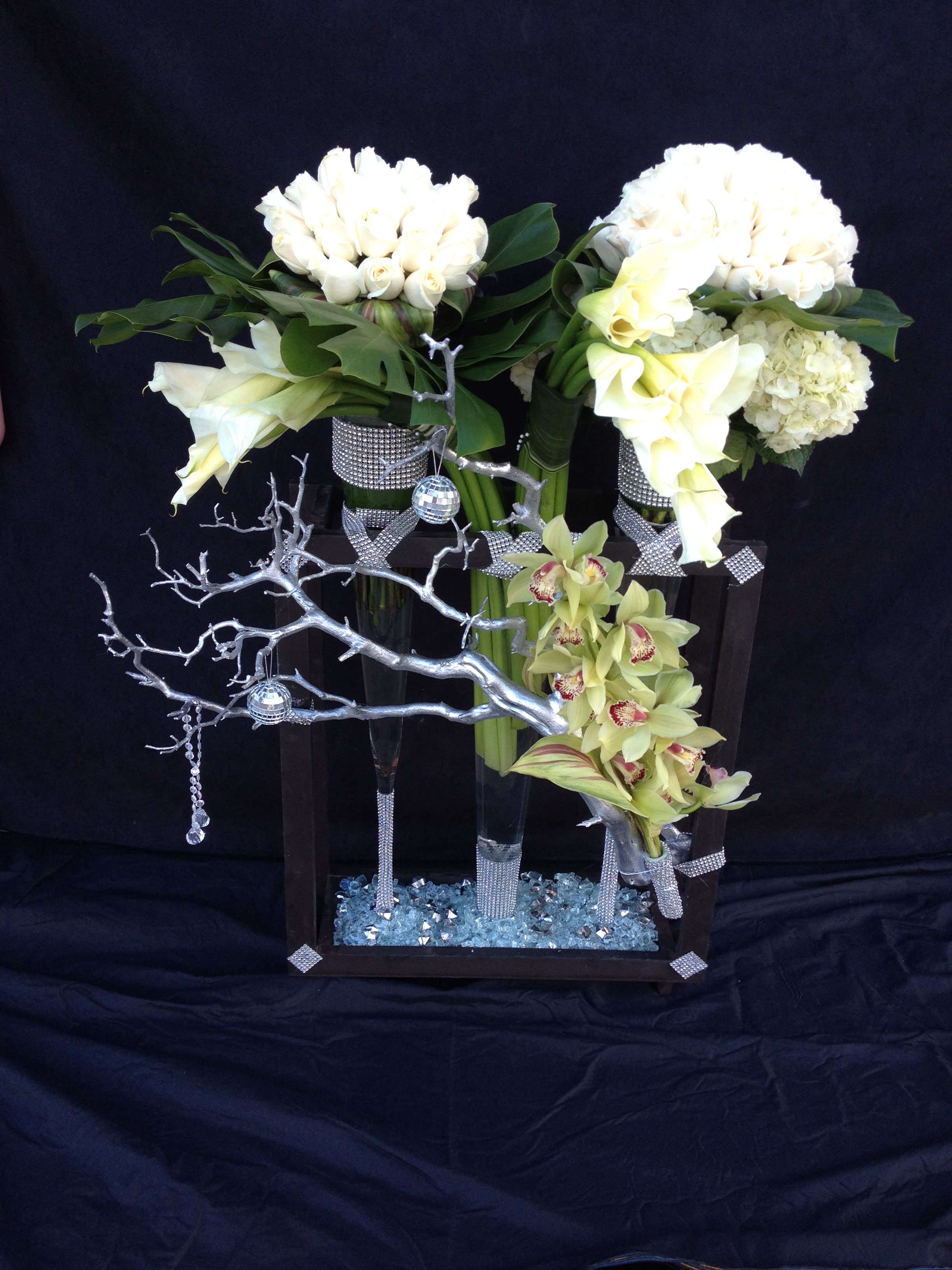 Two white floral arrangements in tall black vases with silver accents