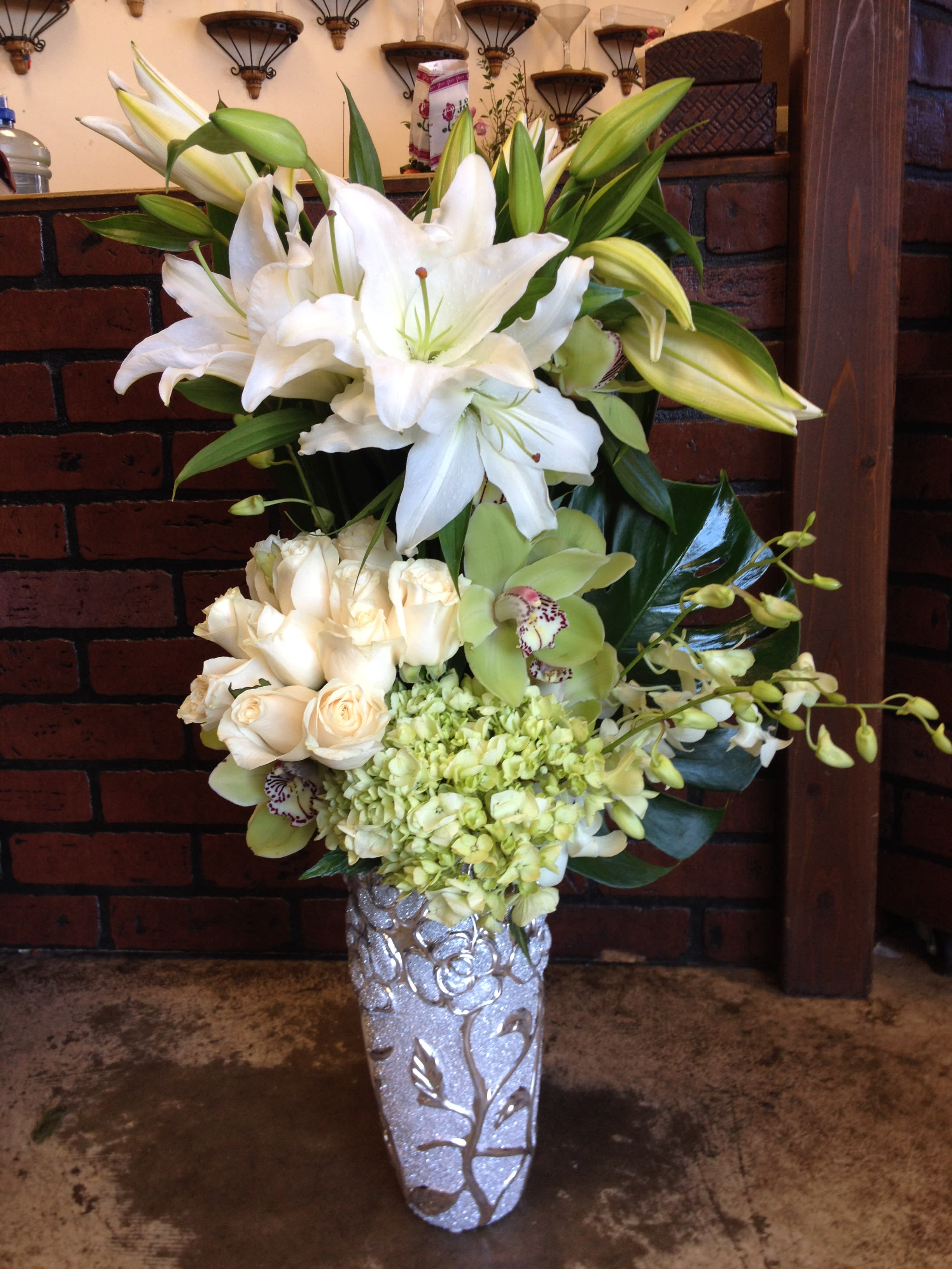 White lilies, cream roses, and green orchids in a silver vase