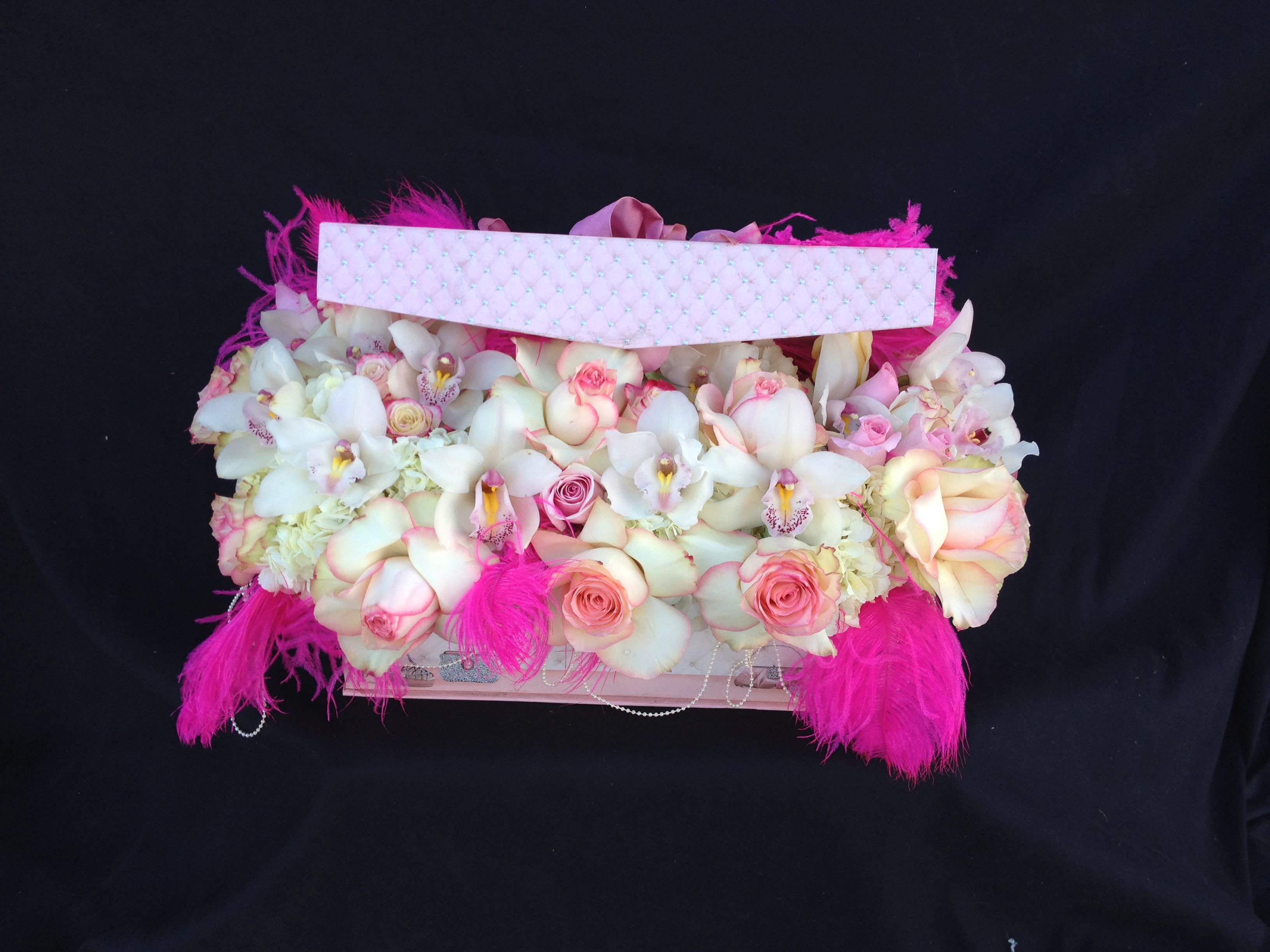 Pink and white floral arrangement in a decorated box with feathers