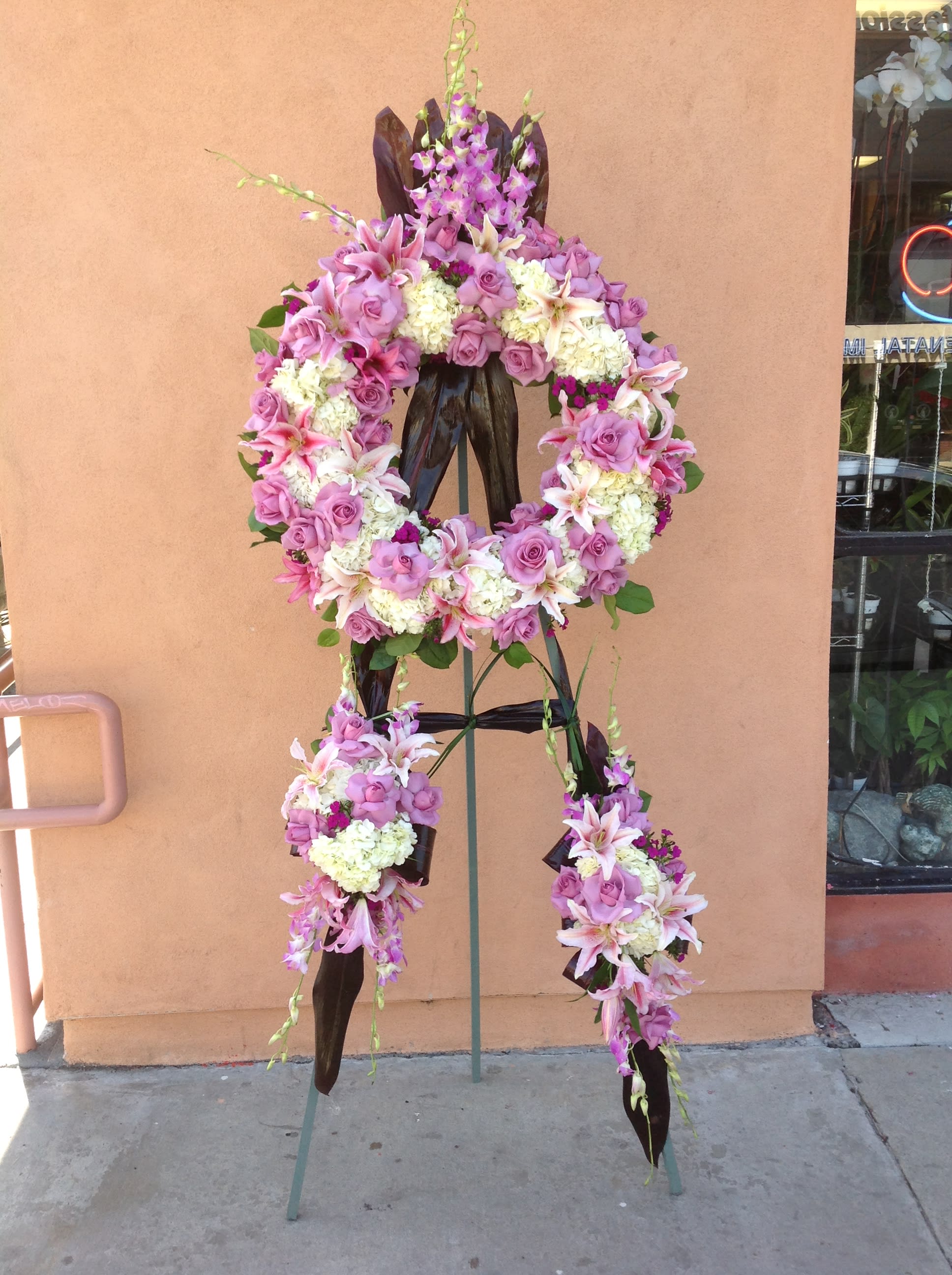 Standing floral wreath with pink roses, lilies, and white blooms on an easel
