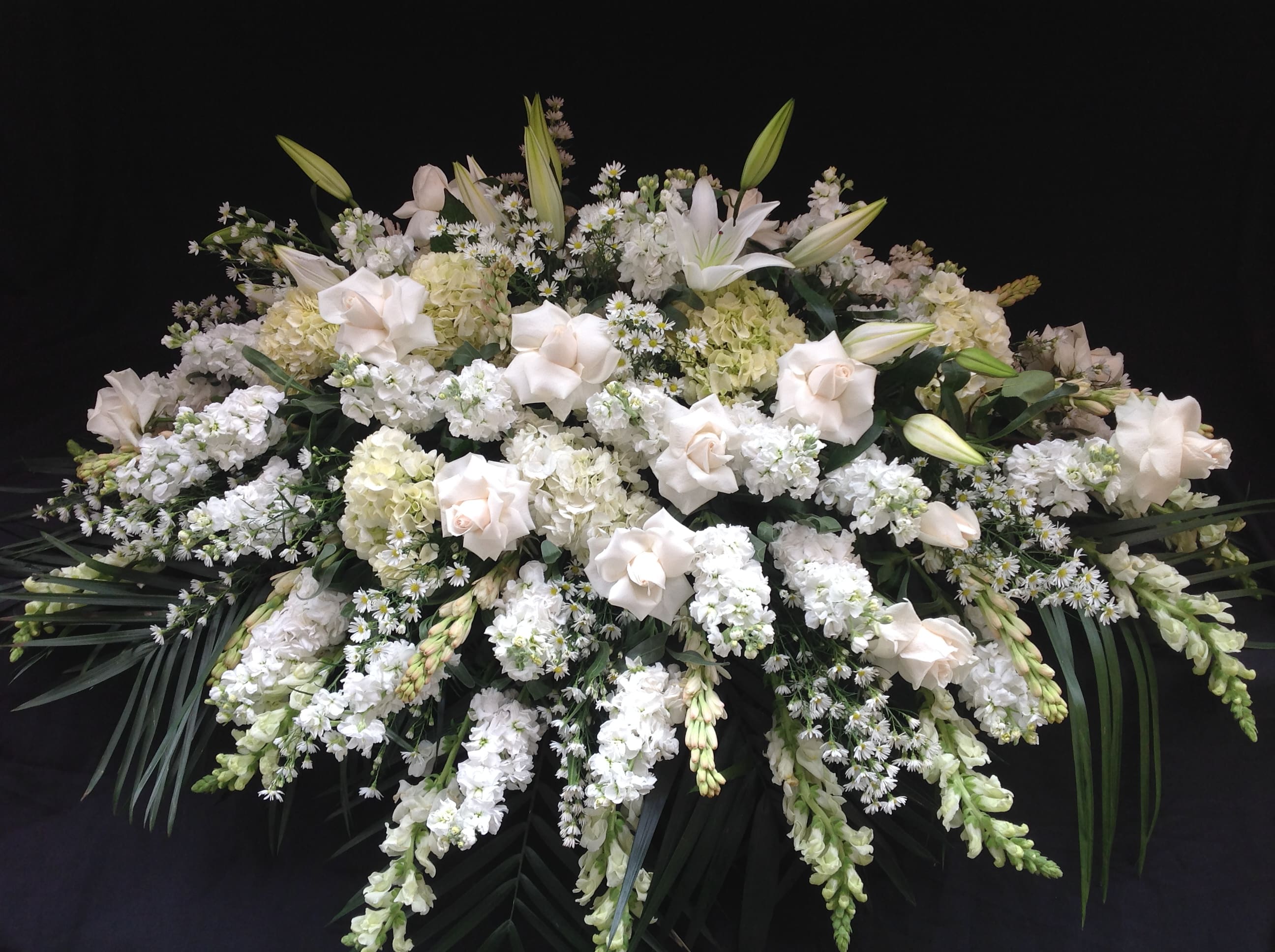 Large white funeral spray with lilies, roses, and clustered white blooms