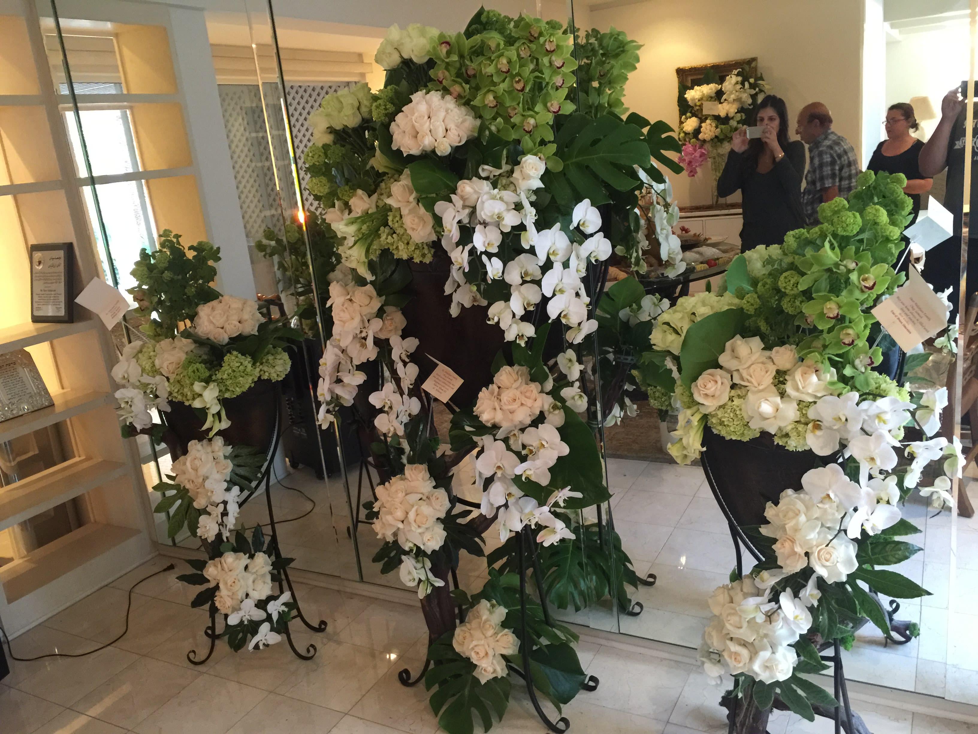 Tall white floral arrangements on black stands in a room