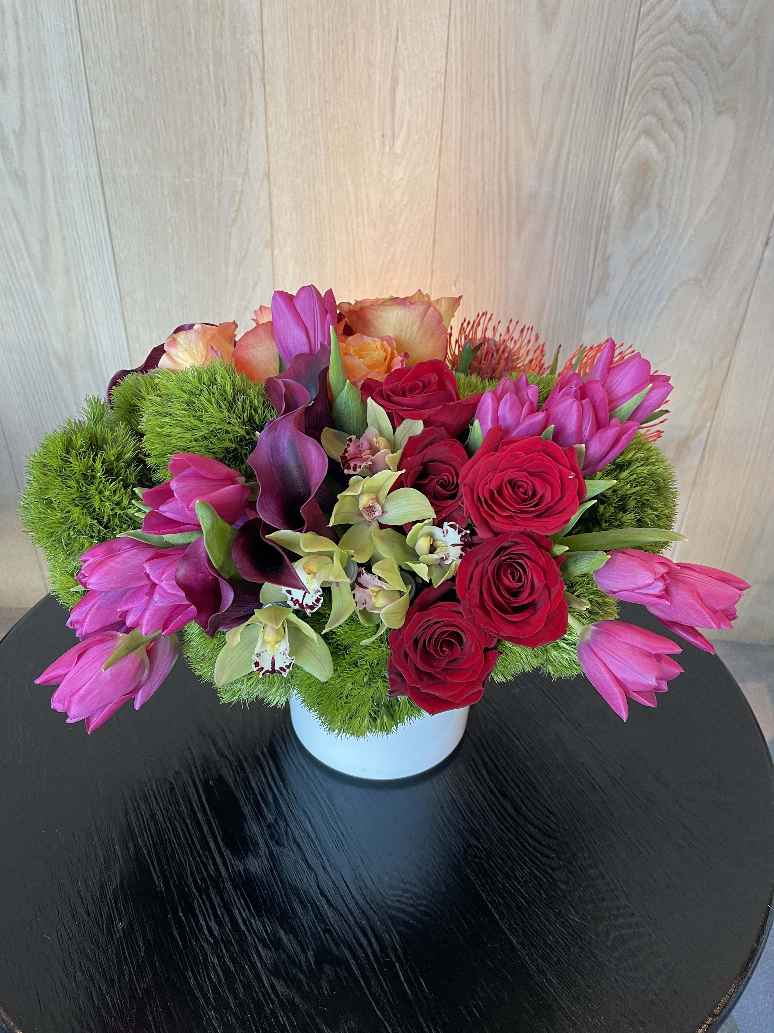 Pink tulips, red roses, and orchids arranged in a white vase