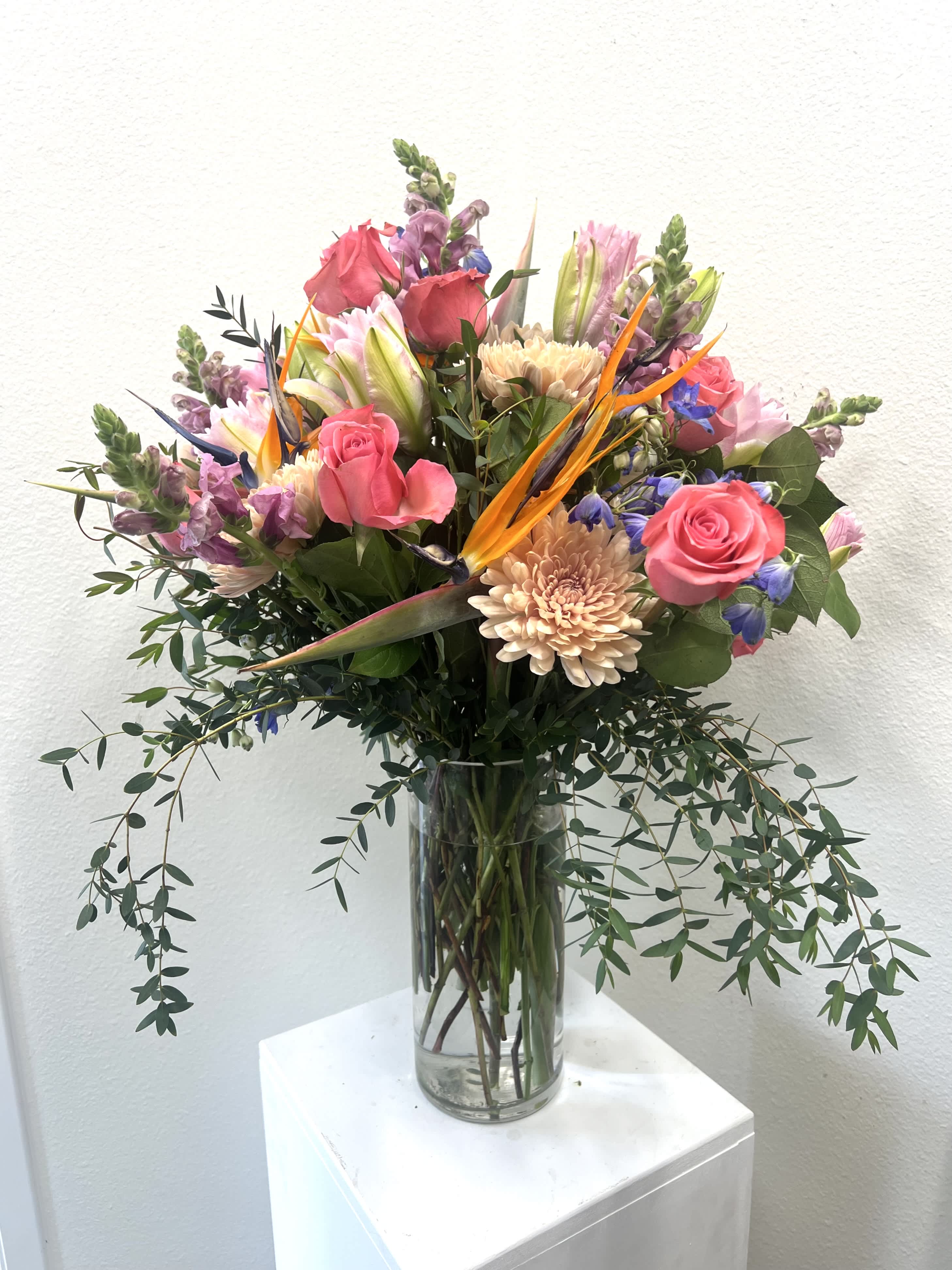 Mixed bouquet of pink roses, lilies, and orange bird of paradise in a glass vase