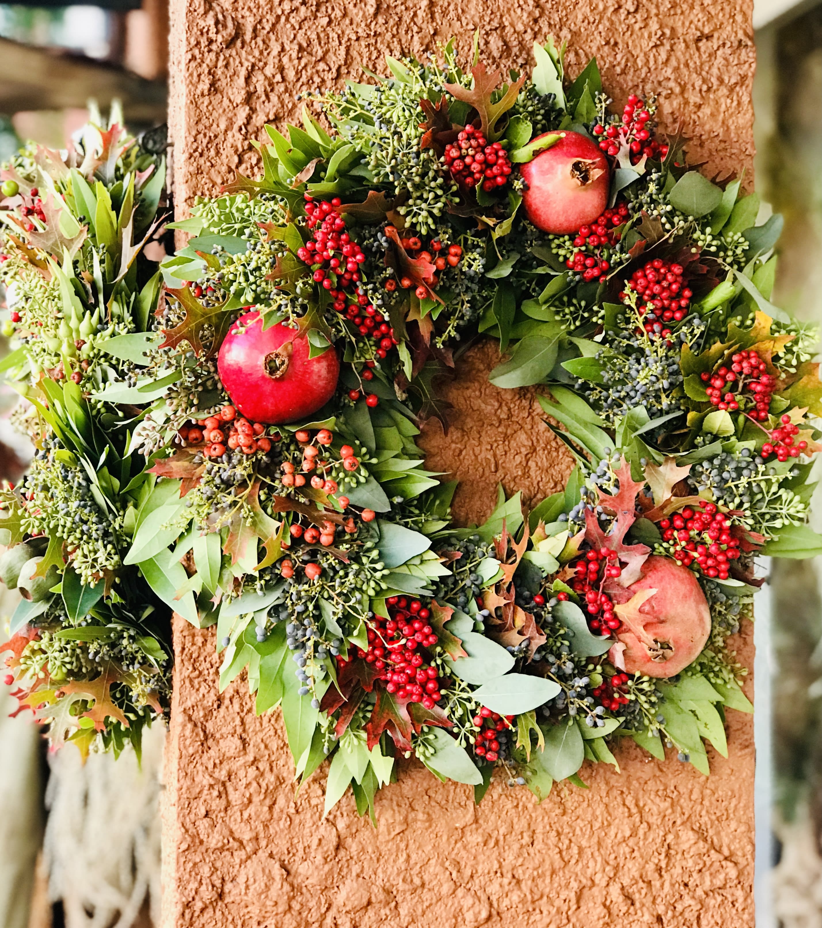 Autumn wreath with red berries and pomegranates on a textured wall