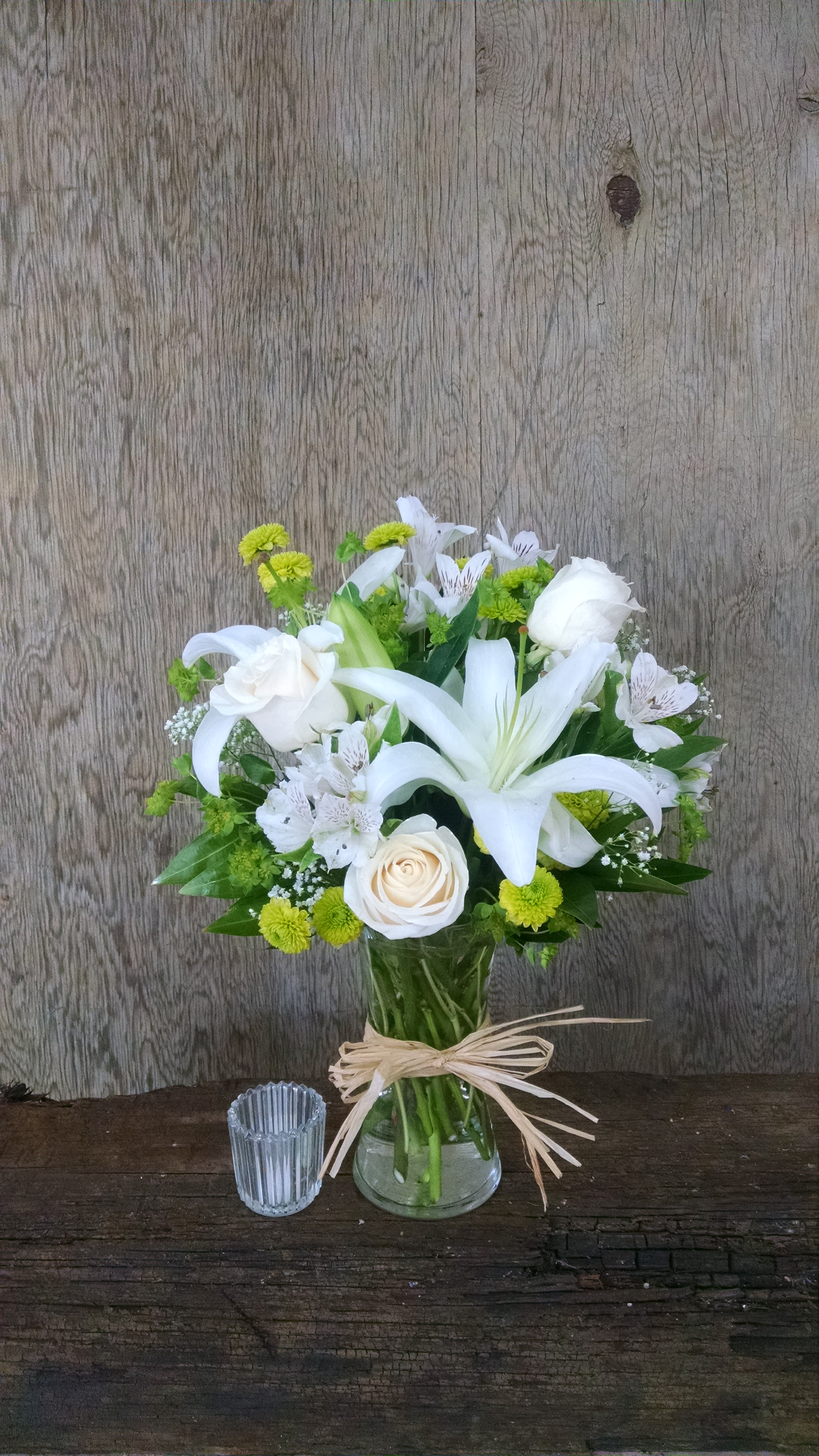 White lilies and roses in a glass vase with green accents
