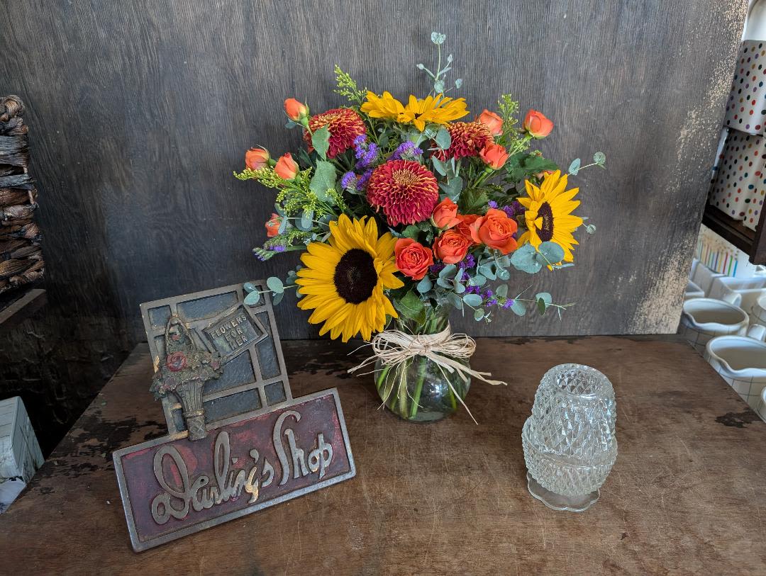 Bouquet of sunflowers, orange roses, and red mums in a glass vase